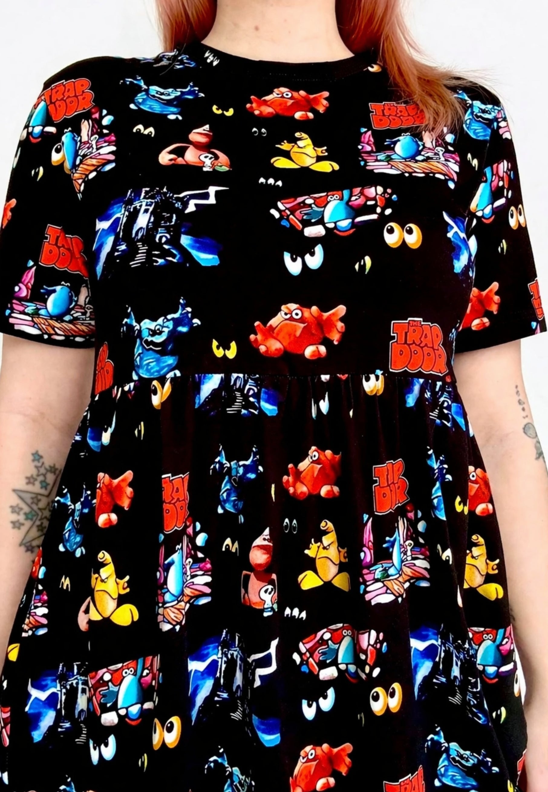 Woman wearing a black dress with a vibrant design of the 1980s children’s tv programme Trap Door. Close up detail of the dress. 