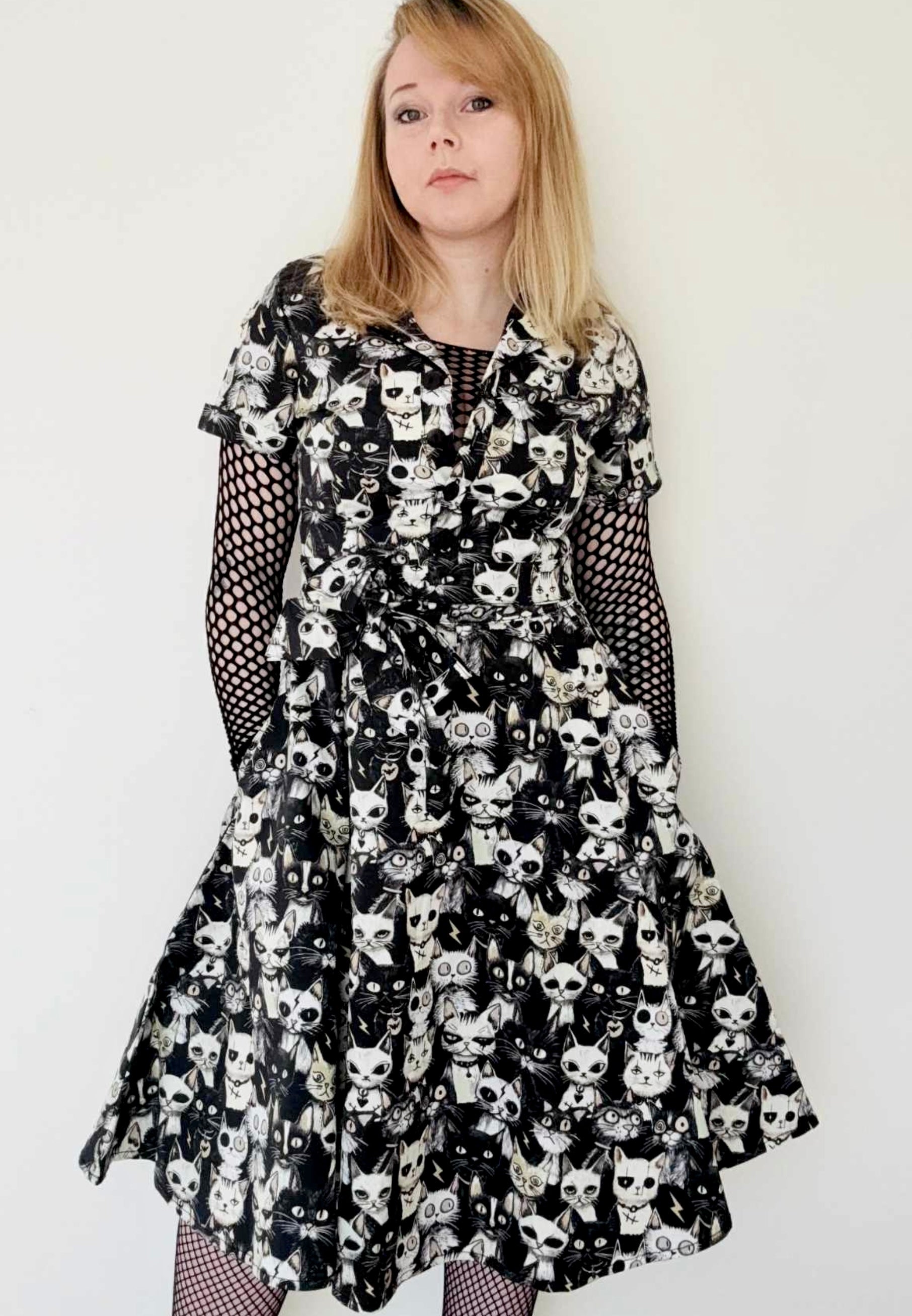 Woman wearing a midi length shirt dress with an alternative print of black, taupe and white alley cats on the fabric. Studio photo