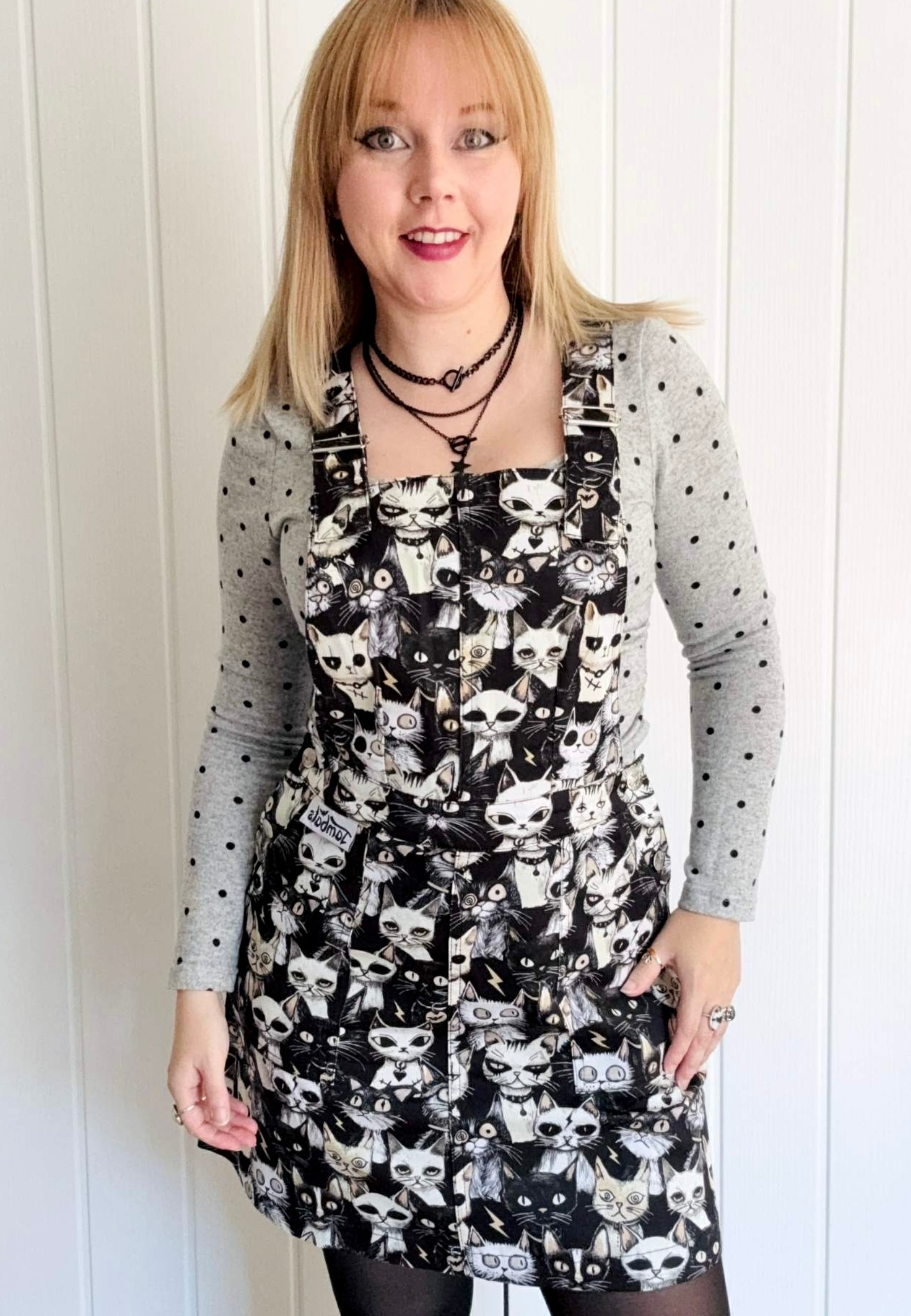 Model wearing a black and white pinafore dress with a print of cute but gothic punky alley cats. Alternative cats print. 