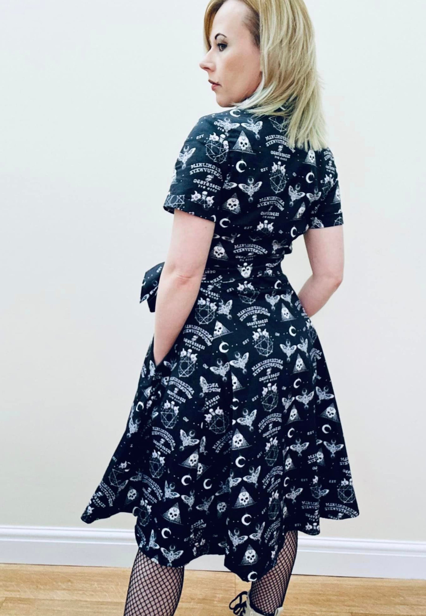 Back view of a woman wearing a black gothic Ouija print dress with a full skirt and button bodice. Image shows the back of the dress