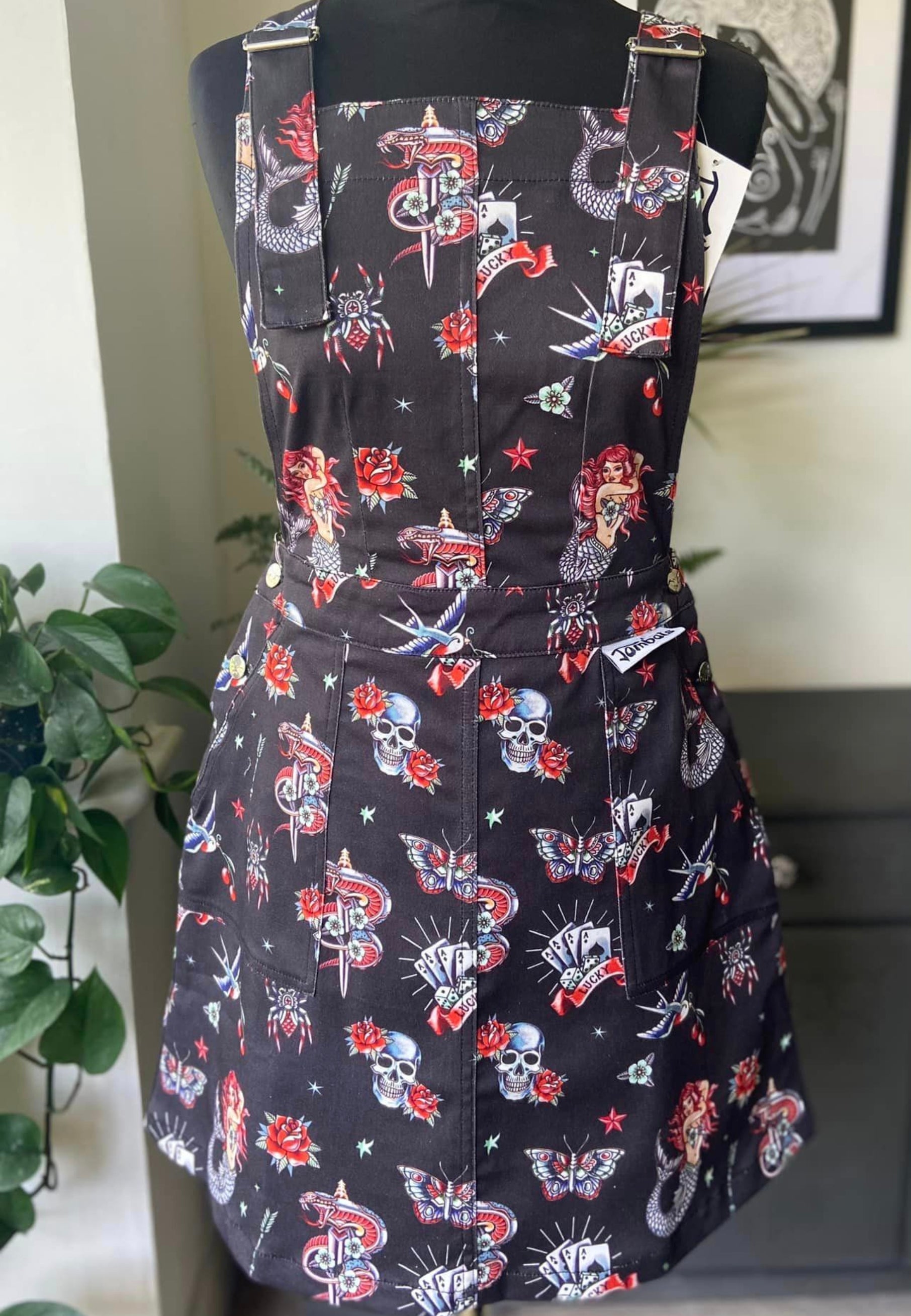 Black pinafore with a detailed fabric print of old school traditional rockabilly retro alternative tattoos. Pinafore in on a mannequin. 