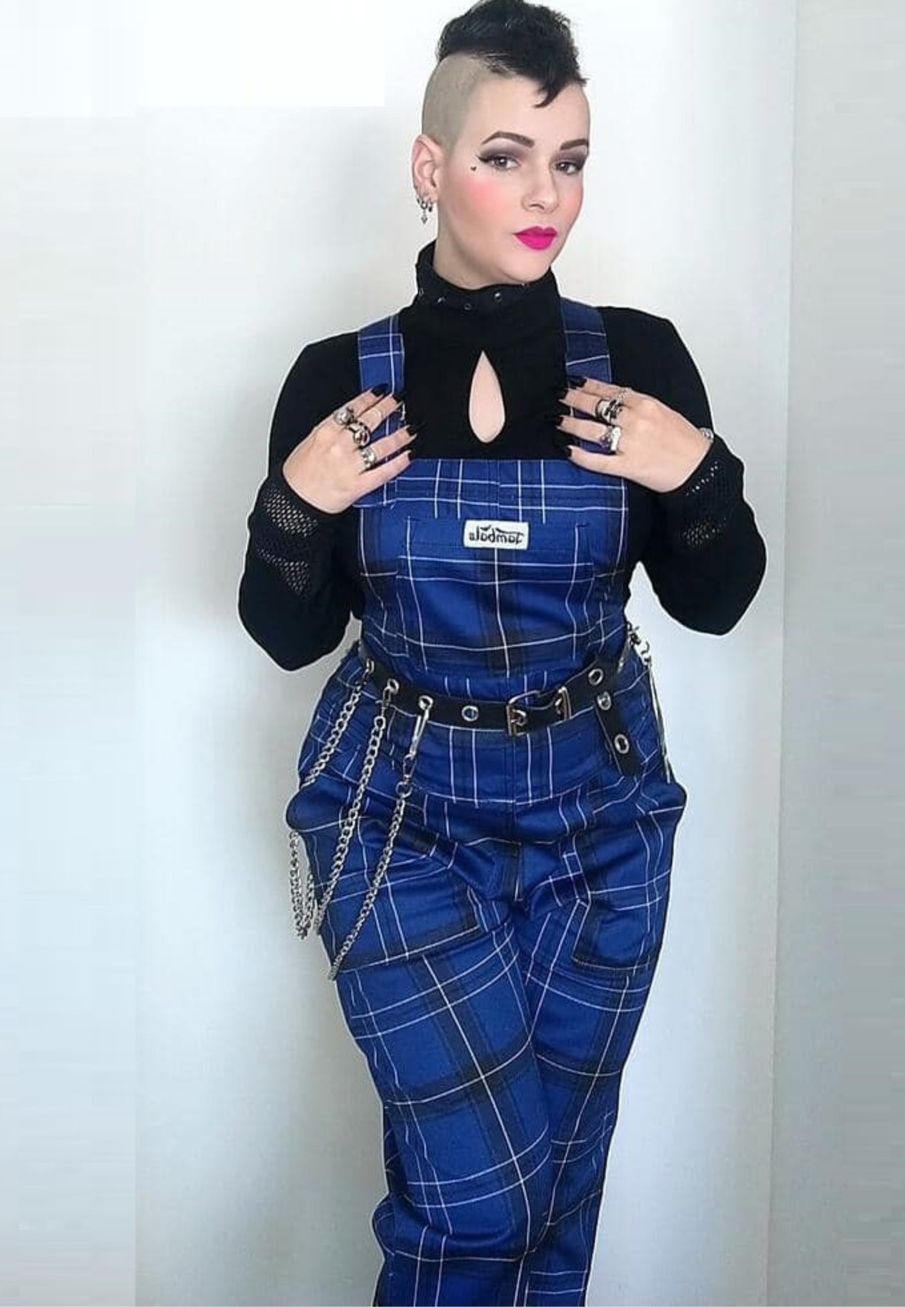 Model in classic dark blue and black tartan dungarees. Studio photo on a plain background. 