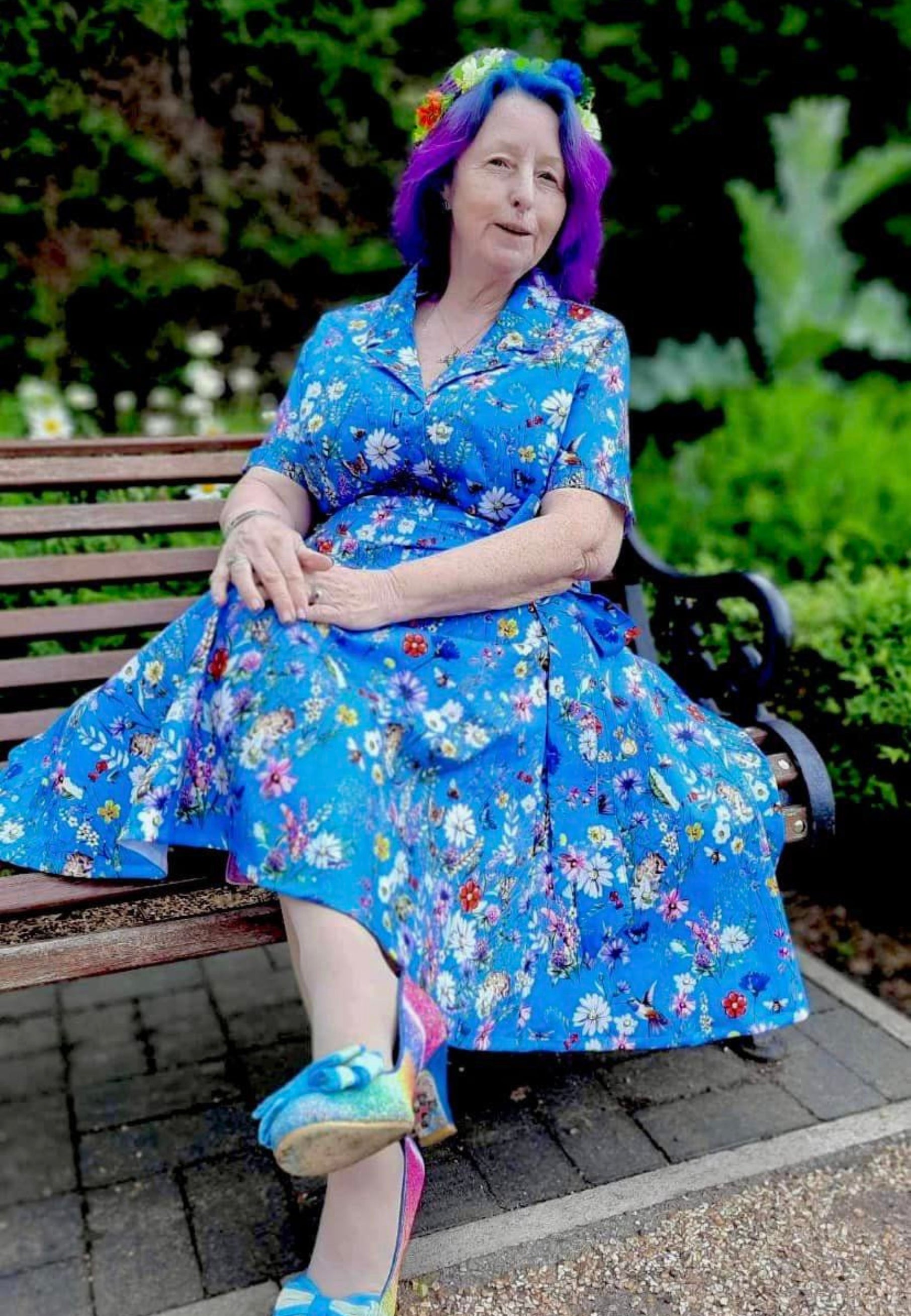 Woman in a beautiful blue retro full skirted dress with pockets and a belt. Print on the dress is a wonderful deep cornflower blue with illustrations of wild meadow flowers and insects, frogs, mice. 