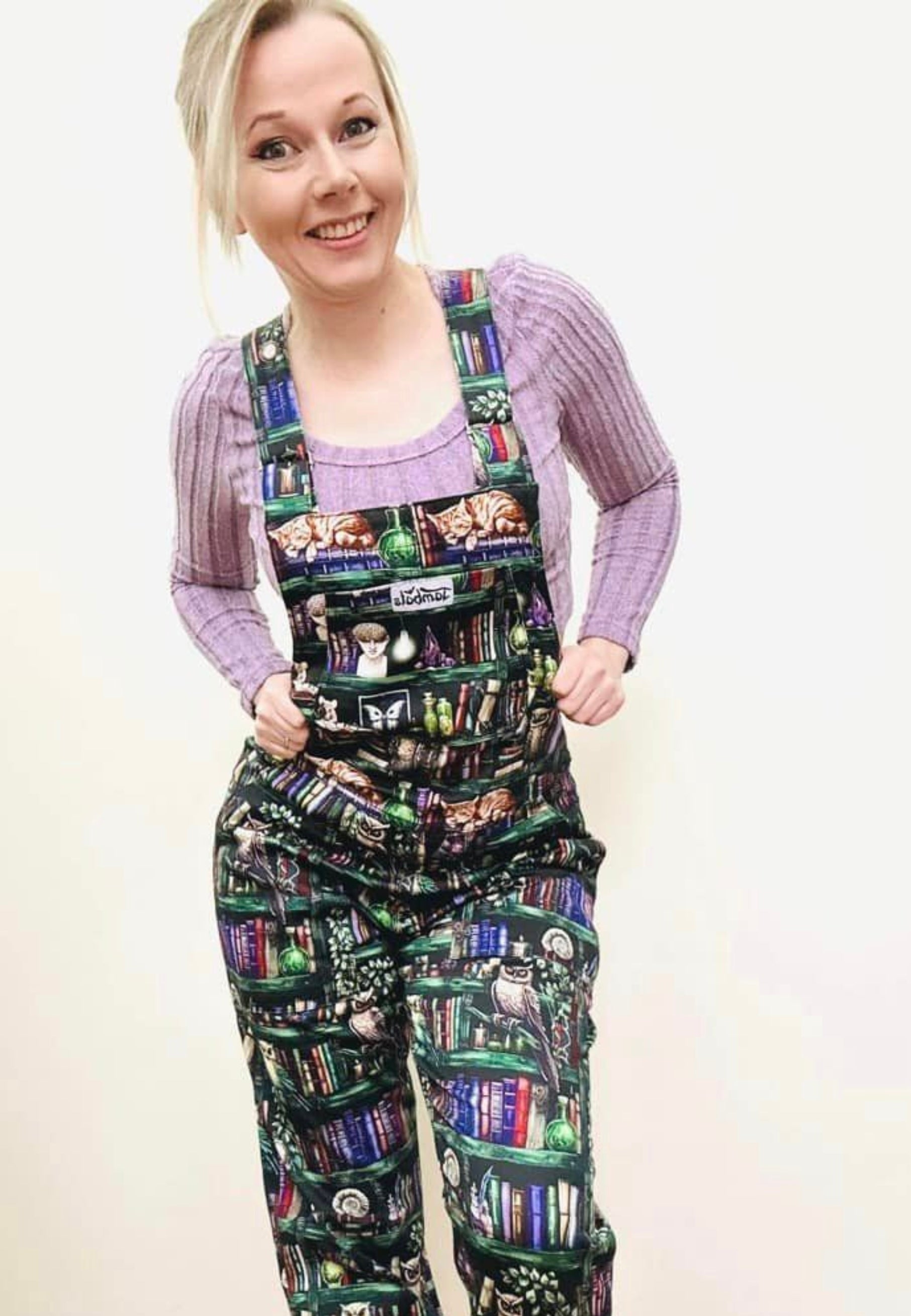 A woman wearing cotton twill dungarees with a unique bookcase and wise owls print. Casually styled. 