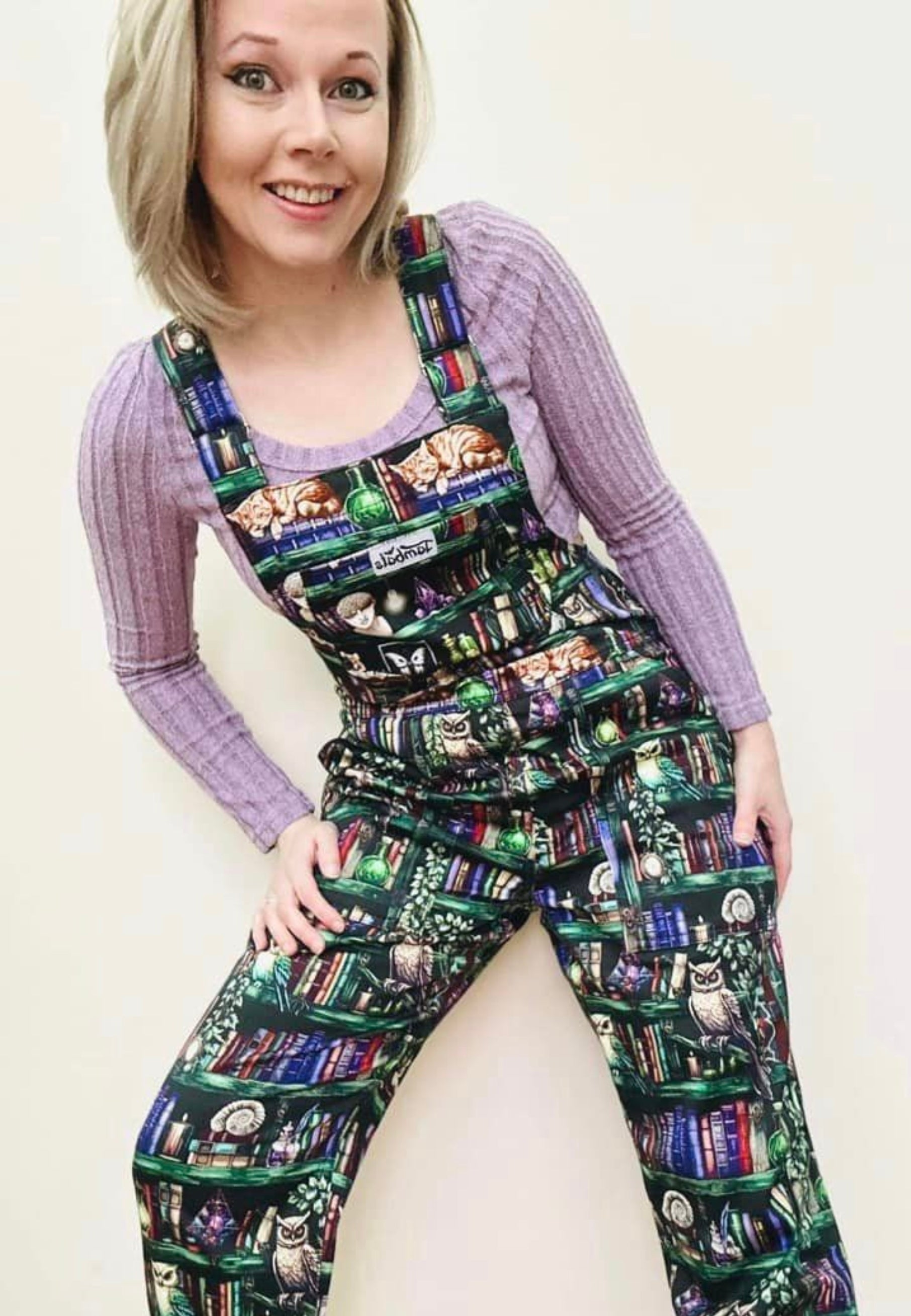 A woman wearing cotton twill dungarees with a unique bookcase and wise owls print. Casually styled. 