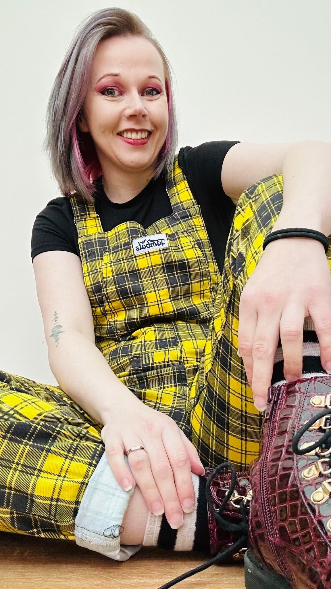 Woman sitting down casually wearing yellow tartan dungaree. Jambats