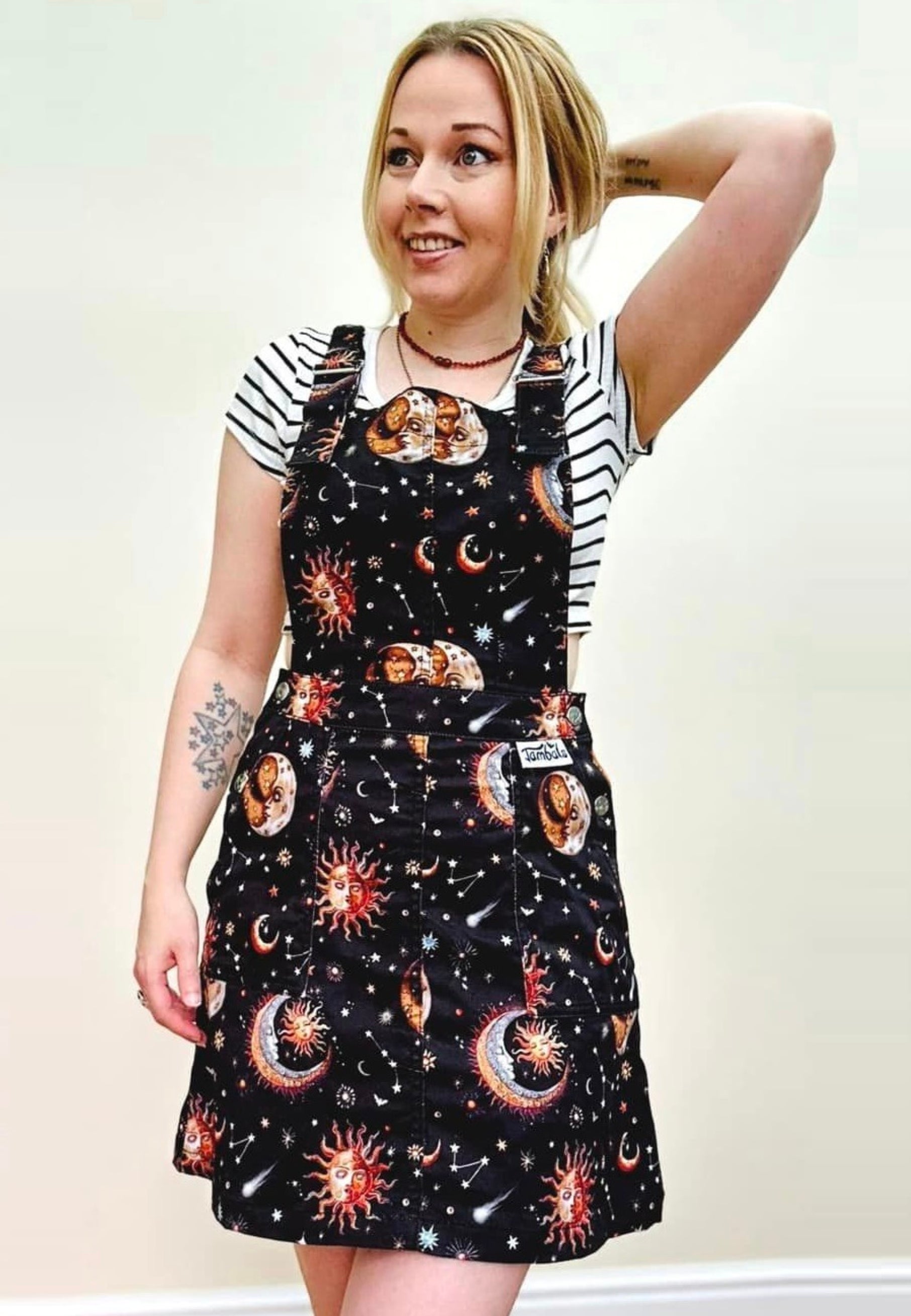 A woman wearing a black pinafore dress with a beautiful celestial print, featuring stars, planets, and moons, paired with a striped top.