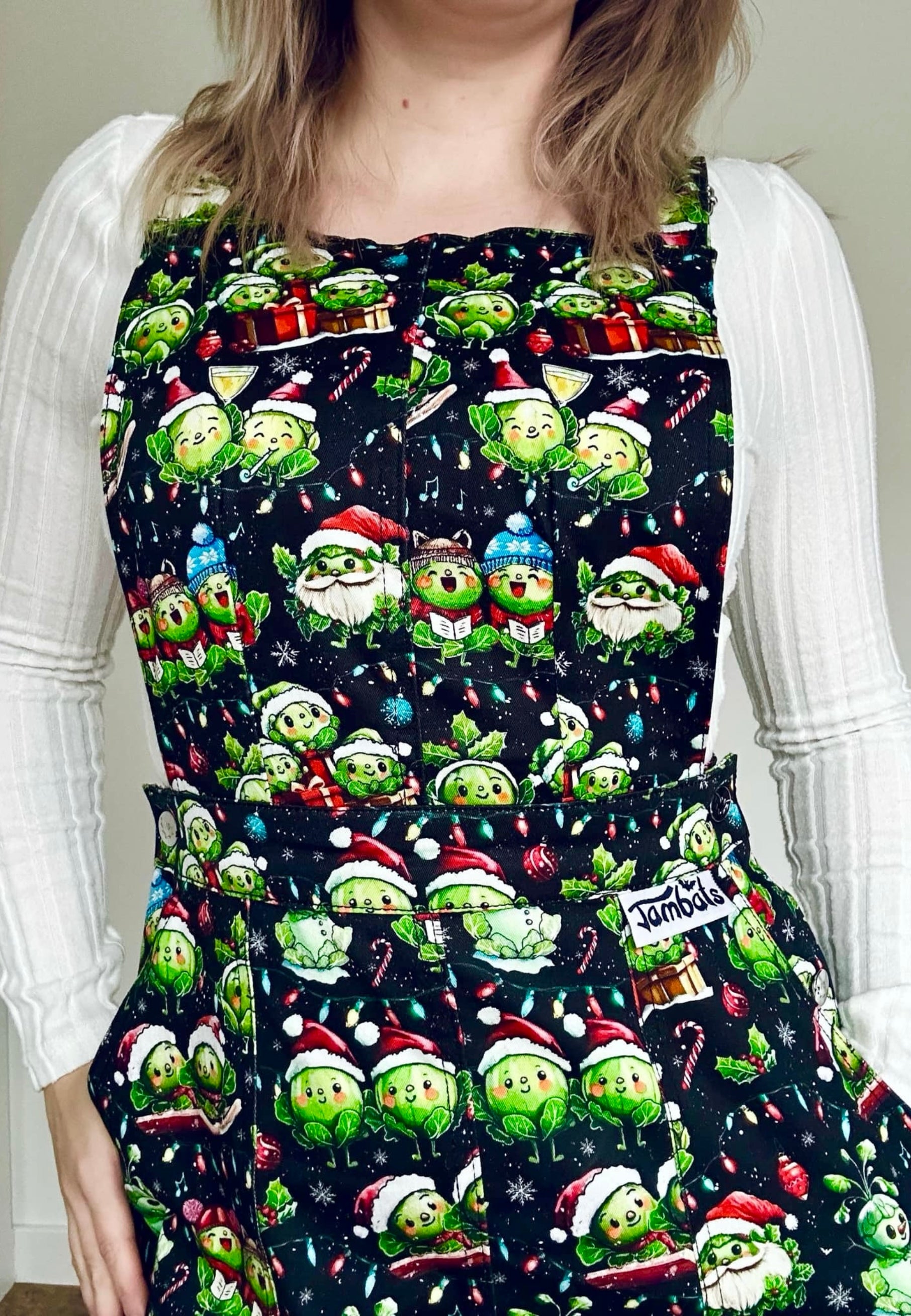 A woman wearing a festive pinafore dress with a pattern of Christmas sprouts. From carol singing to snowman building, Christmas partying to snow sledging… cheeky Sprouts celebrating the season. 