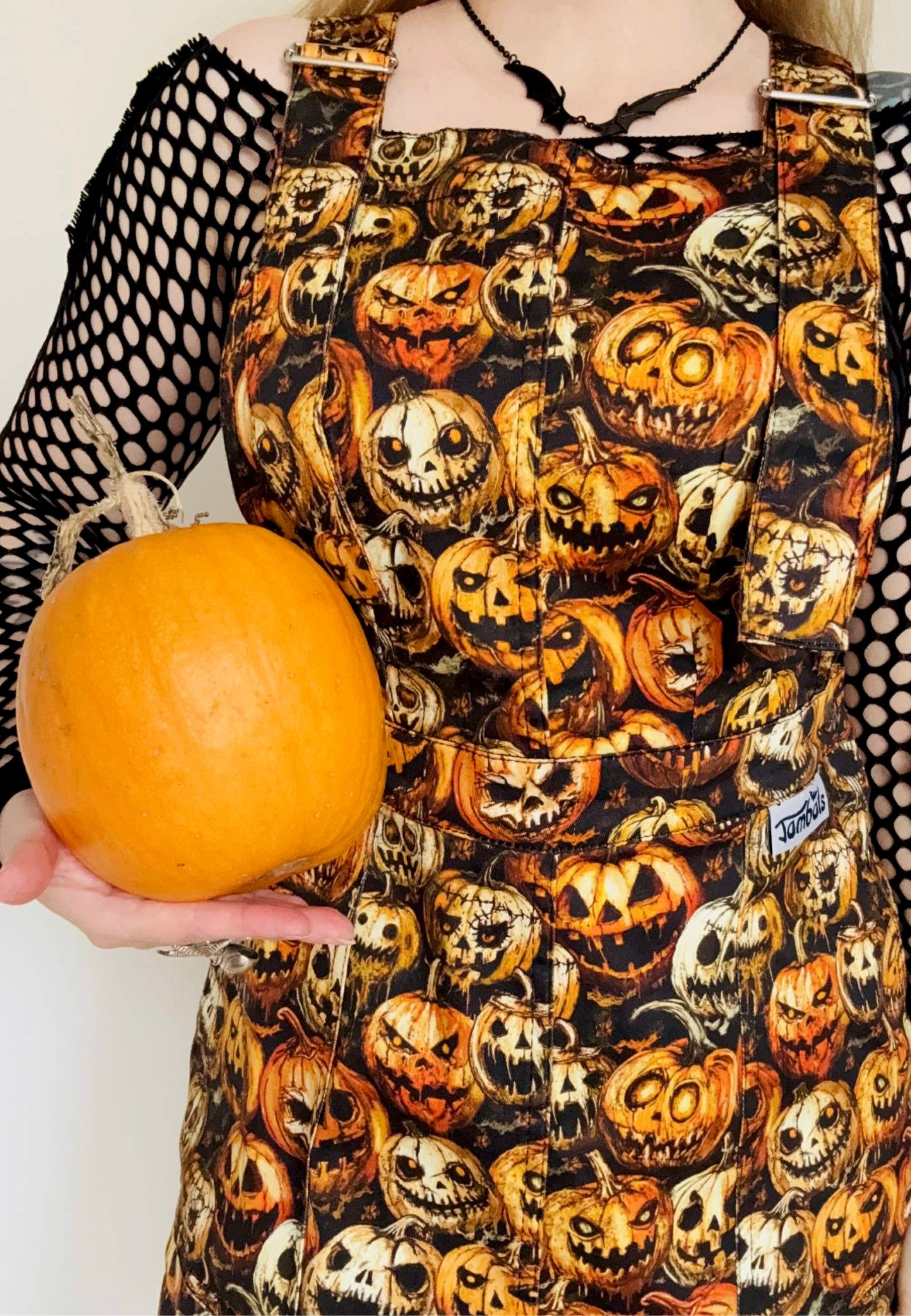 Close up of a spooky pinafore dress with creepy pumpkins print. Studio photo. Model is holding a pumpkin. 