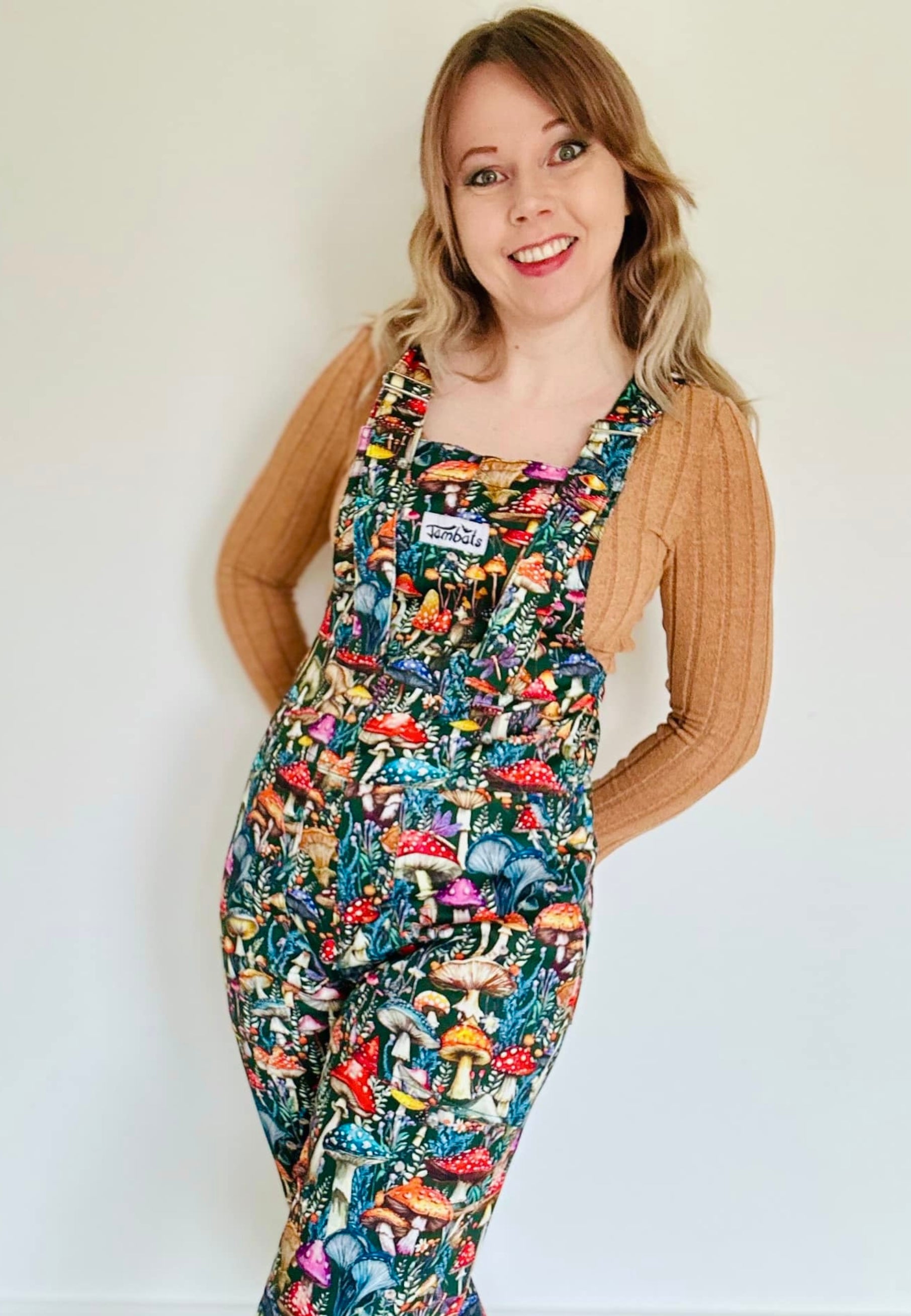 A woman wearing a pair of vibrantly patterned dungarees with a beautiful mushroom design, standing against a plain background.
