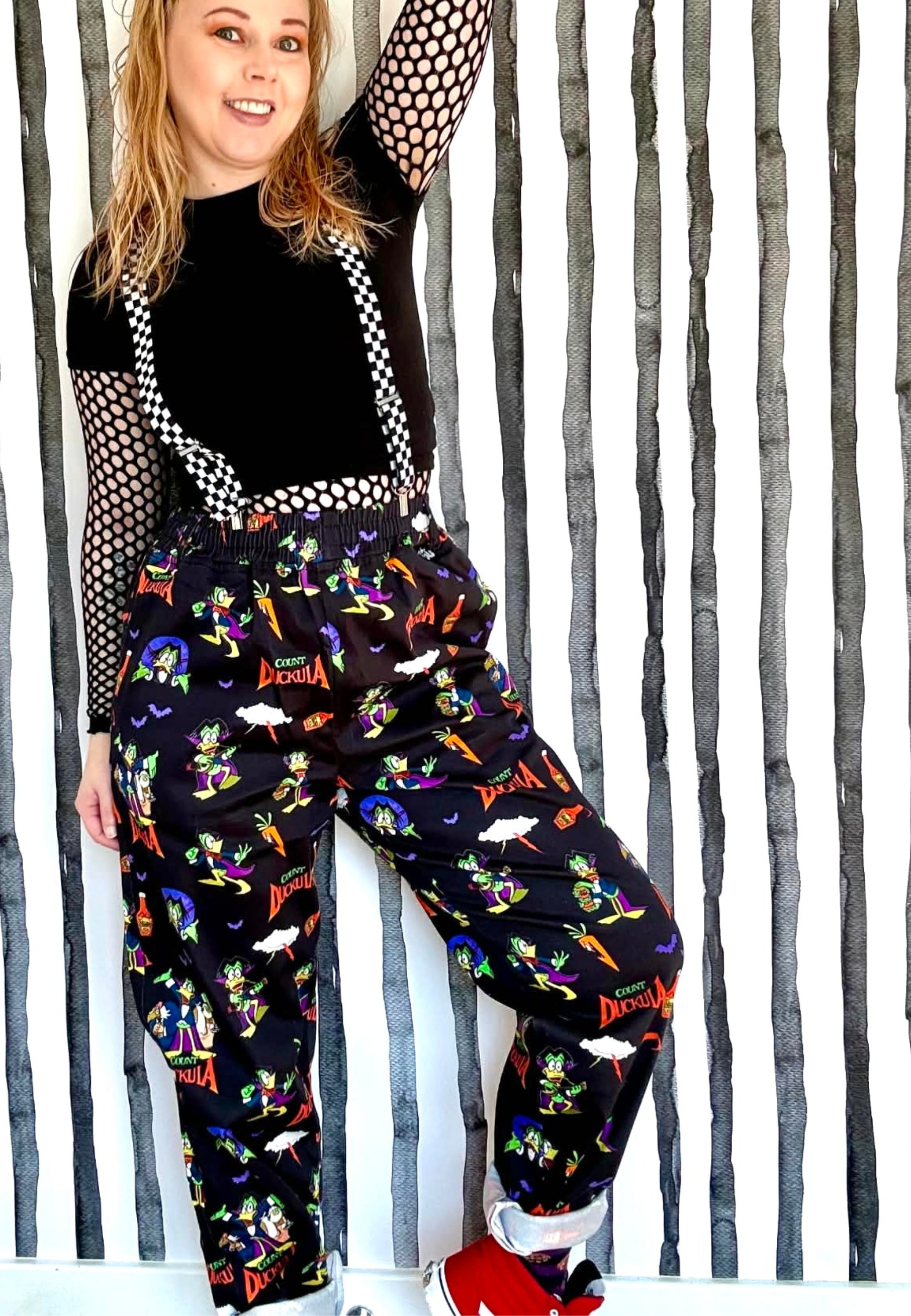 Person wearing colourful Count Duckula print trousers with a black top and red shoes against a striped background