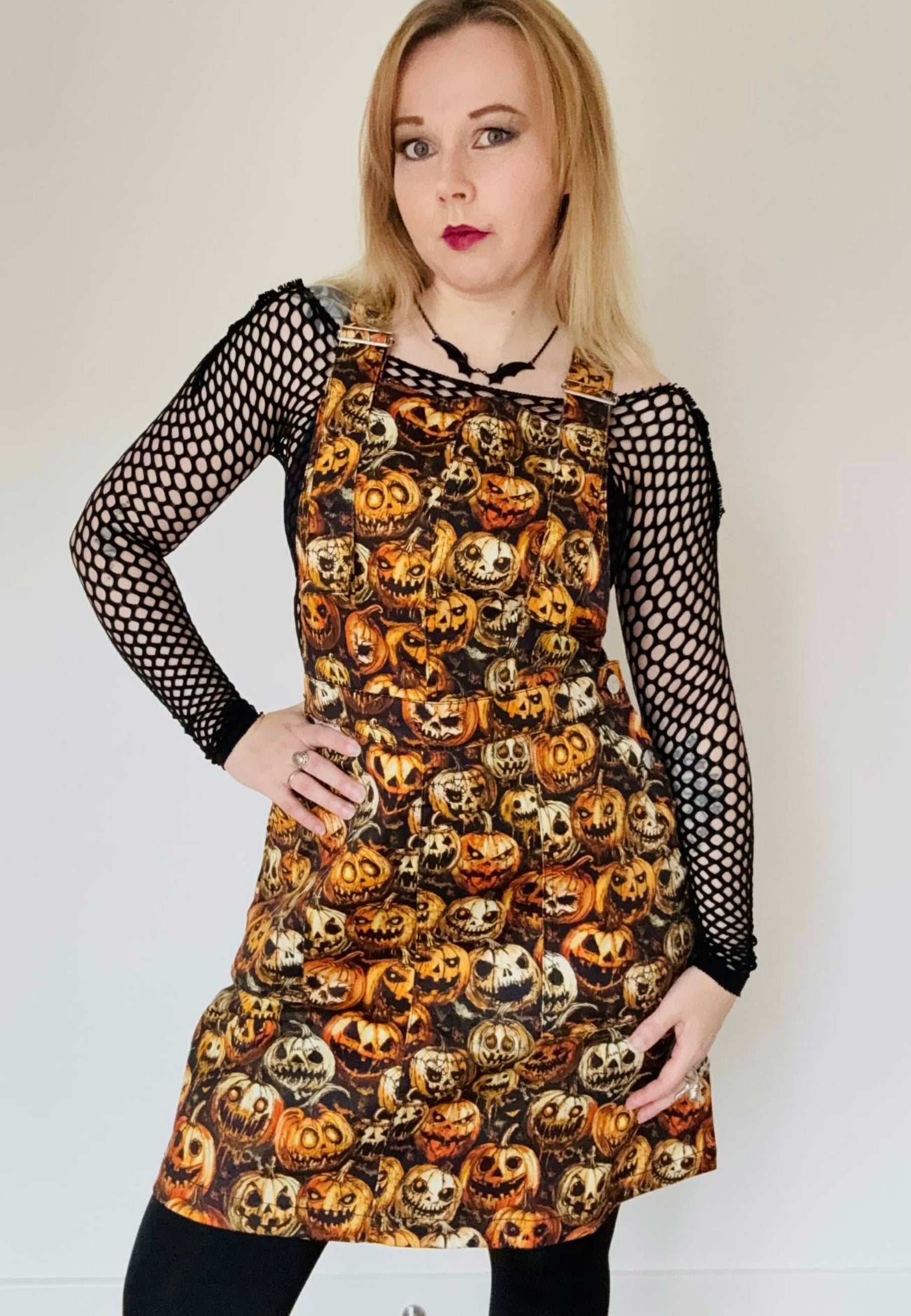 Woman wearing a spooky pinafore dress with creepy pumpkins print. Studio photo. 