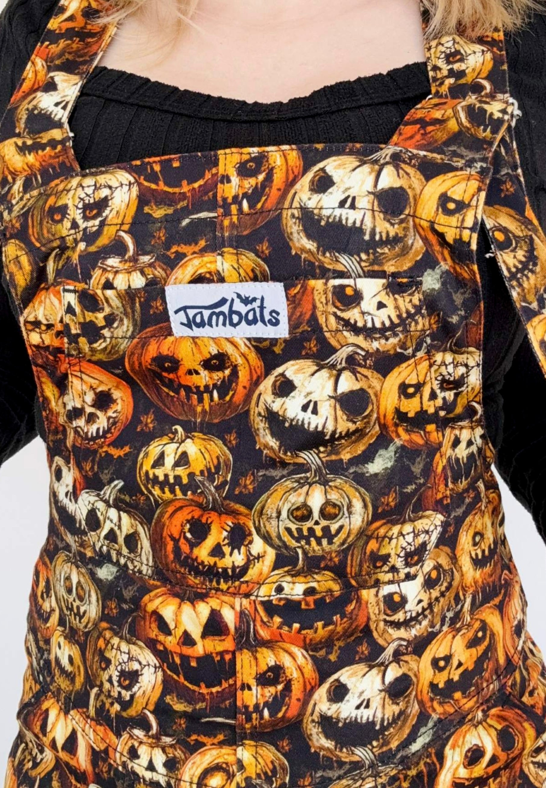 Close up of Halloween themed dungarees or overalls with pumpkins and jack-o'-lantern design and  a 'Jambals' brand label.