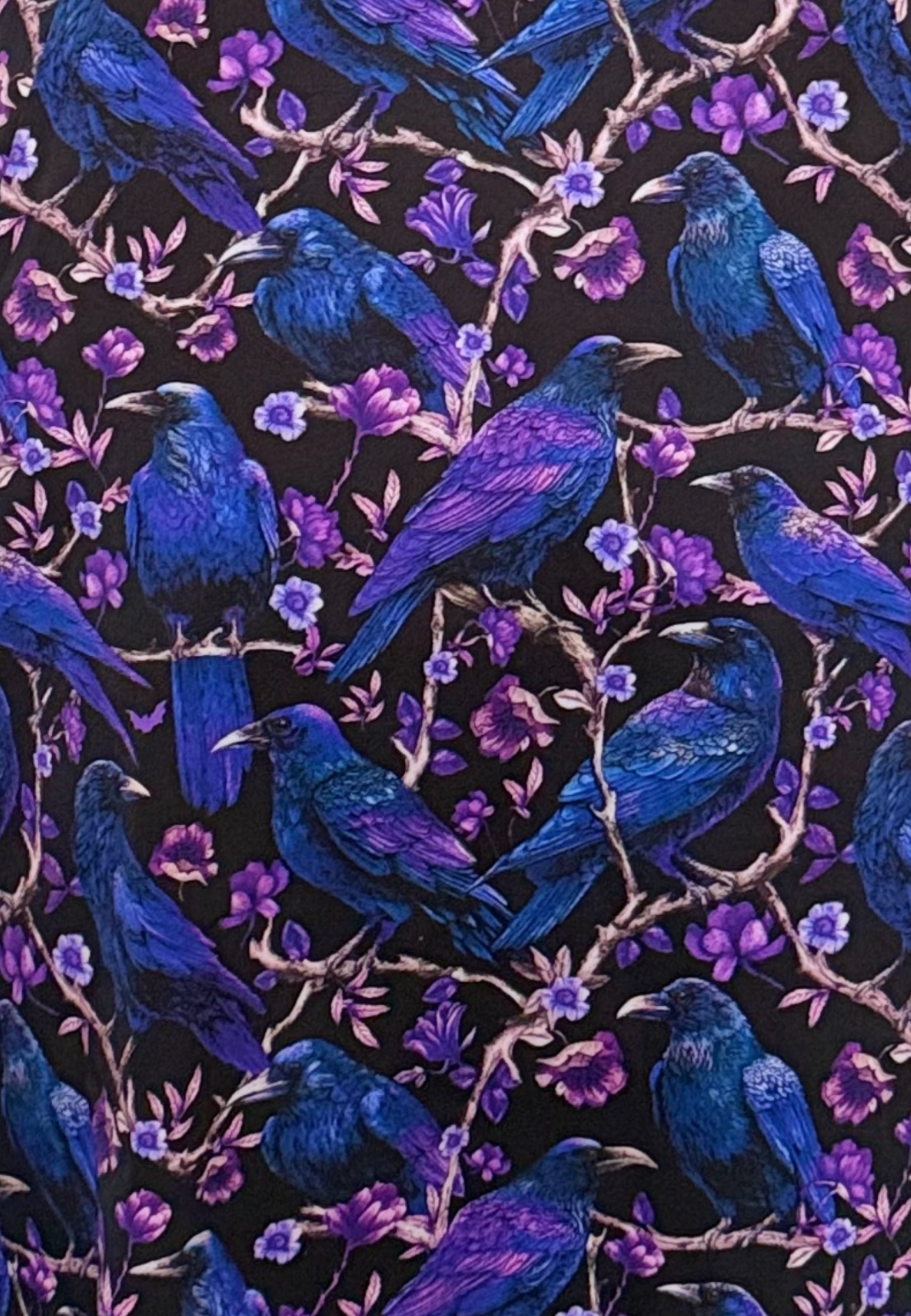Close up of a beautiful fabric print of ravens and crows perched on blooming branches. Deep purples and blues on black. 