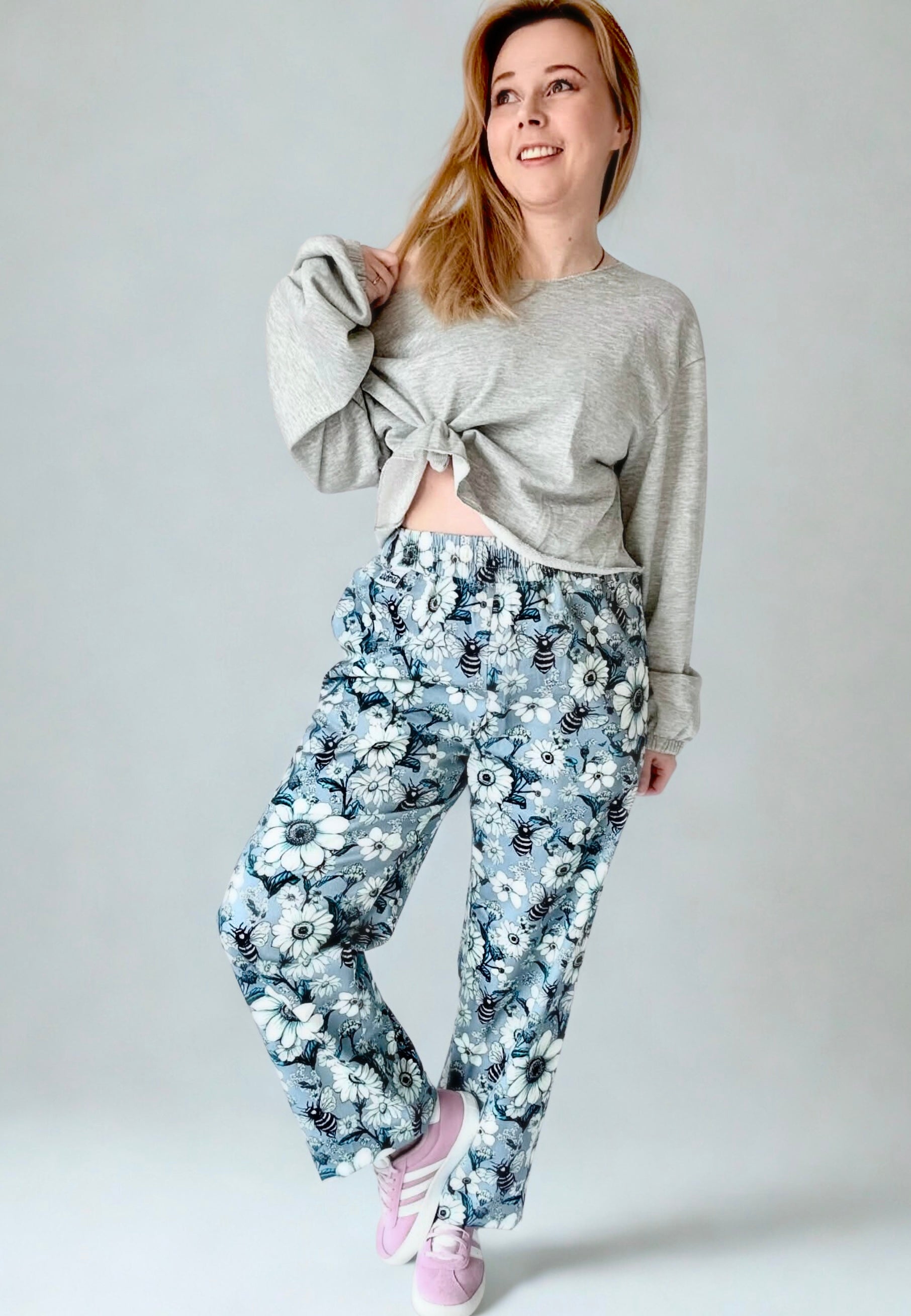 Woman wearing a grey sweater and grey trousers with a print of retro daisies and bees. Photo on a plain studio background 