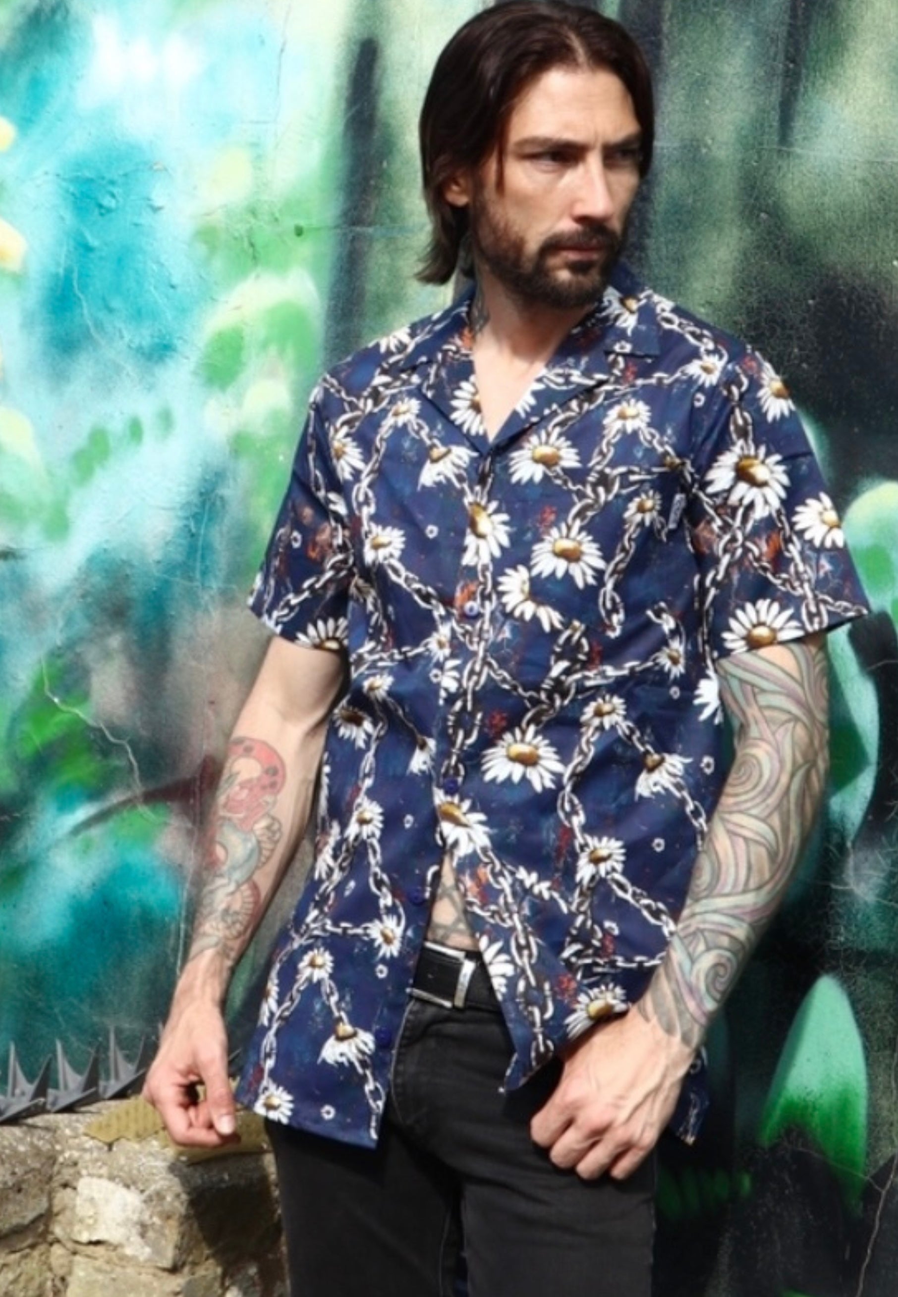 Man wearing a blue shirt with a daisy and urban grungey chains prong against a colorful mural background