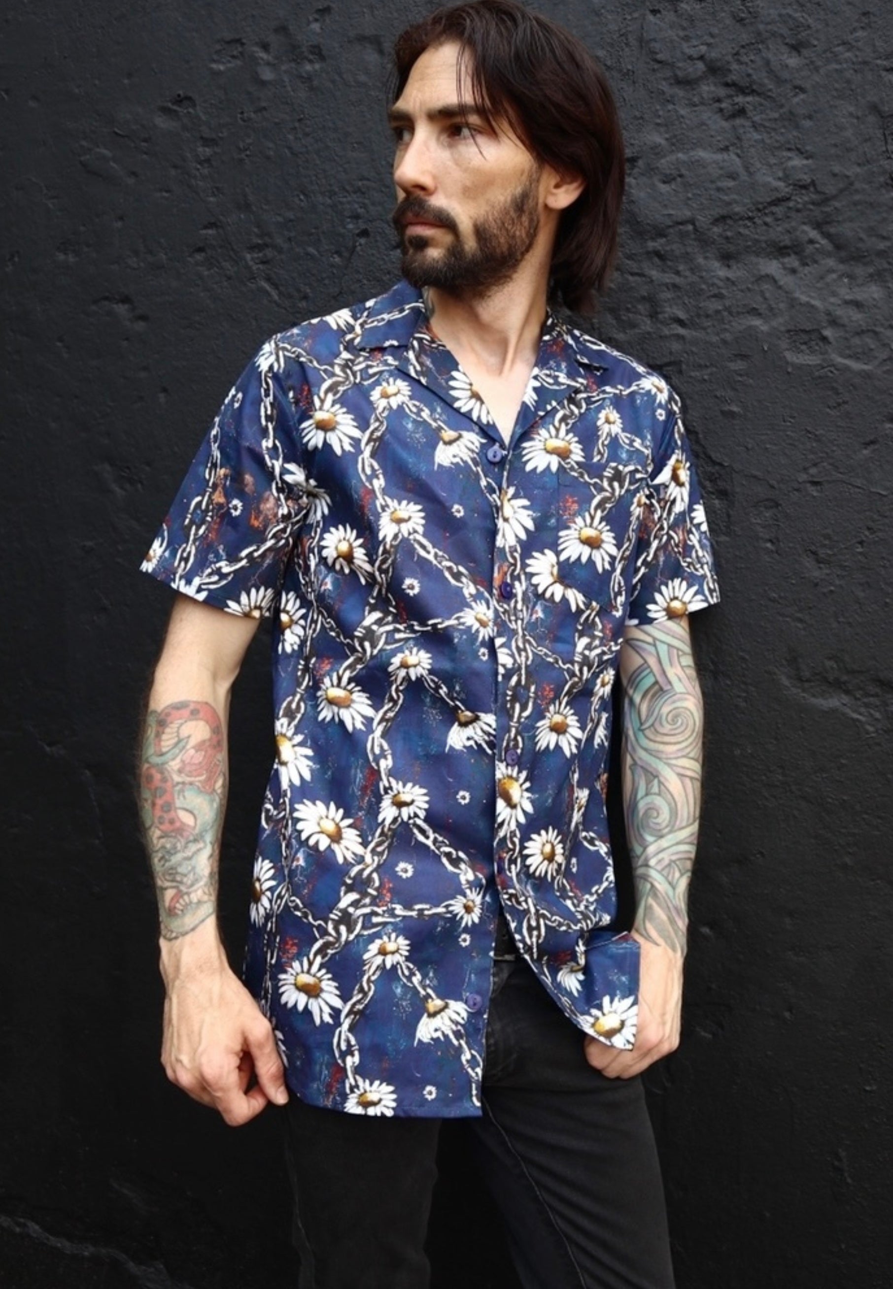 Man wearing a blue floral daisies and grungey chains patterned shirt against a black background