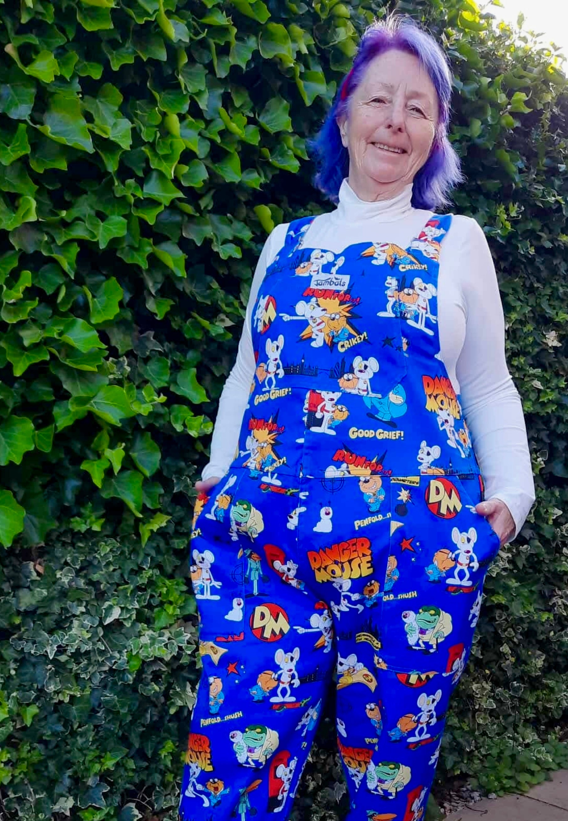 Woman wearing blue Danger Mouse dungarees with a yellow top underneath. Outdoor photo. 
