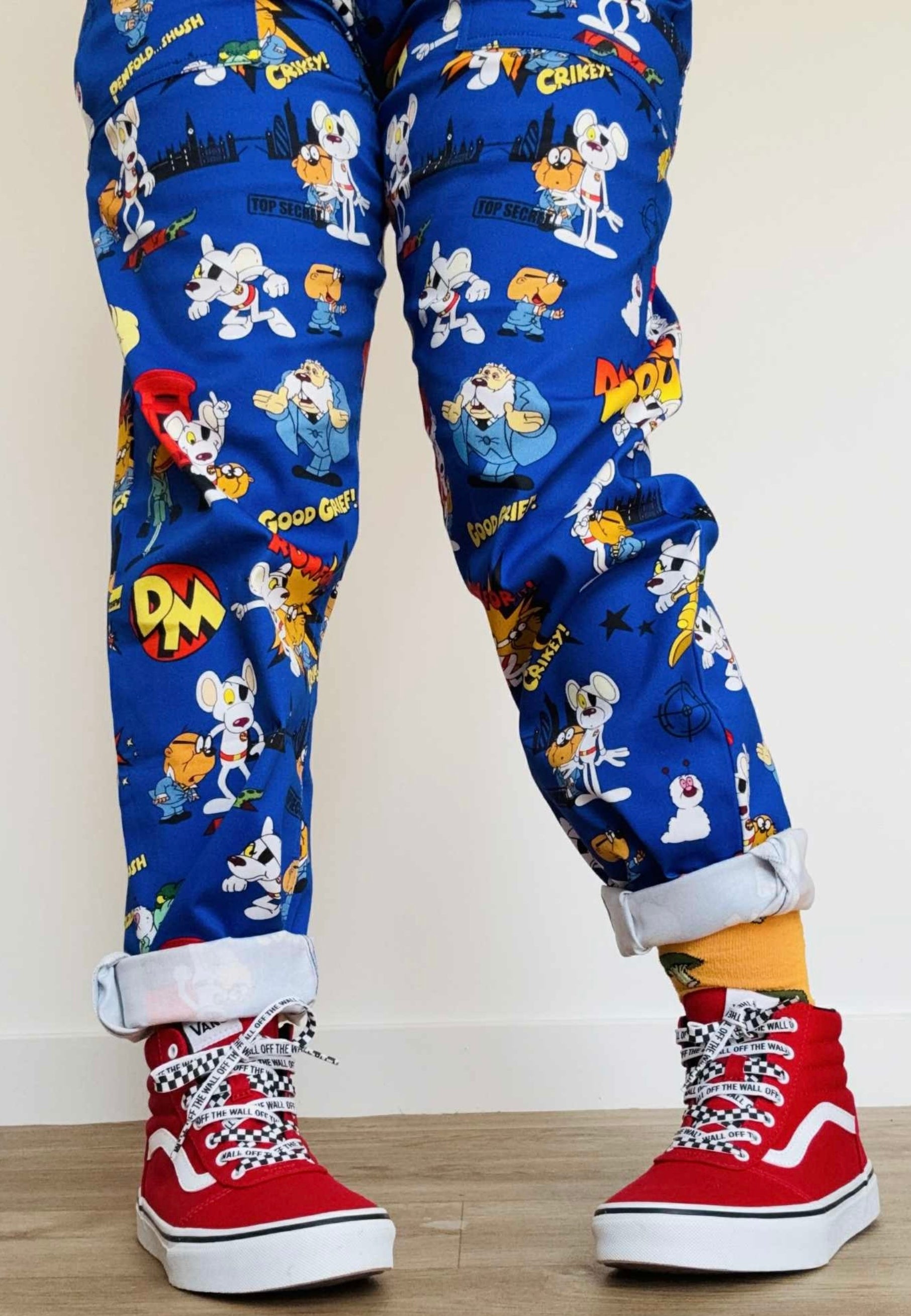 Blue dungaree trousers with Danger Mouse pattern worn with red high-top sneakers on a plain background