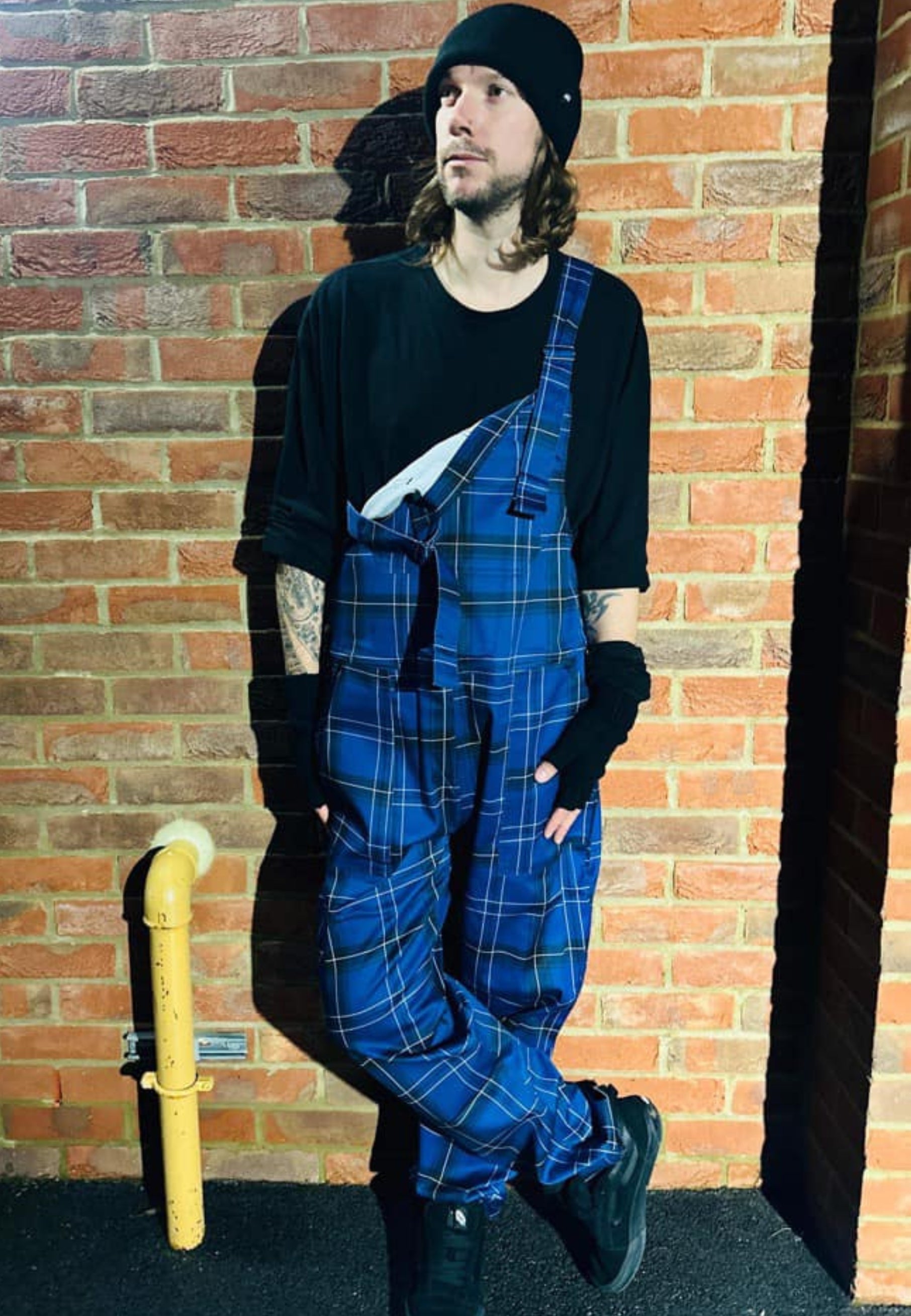 Man in classic dark blue and black tartan dungarees, worn really loose with one strap down. Outdoor evening photo  