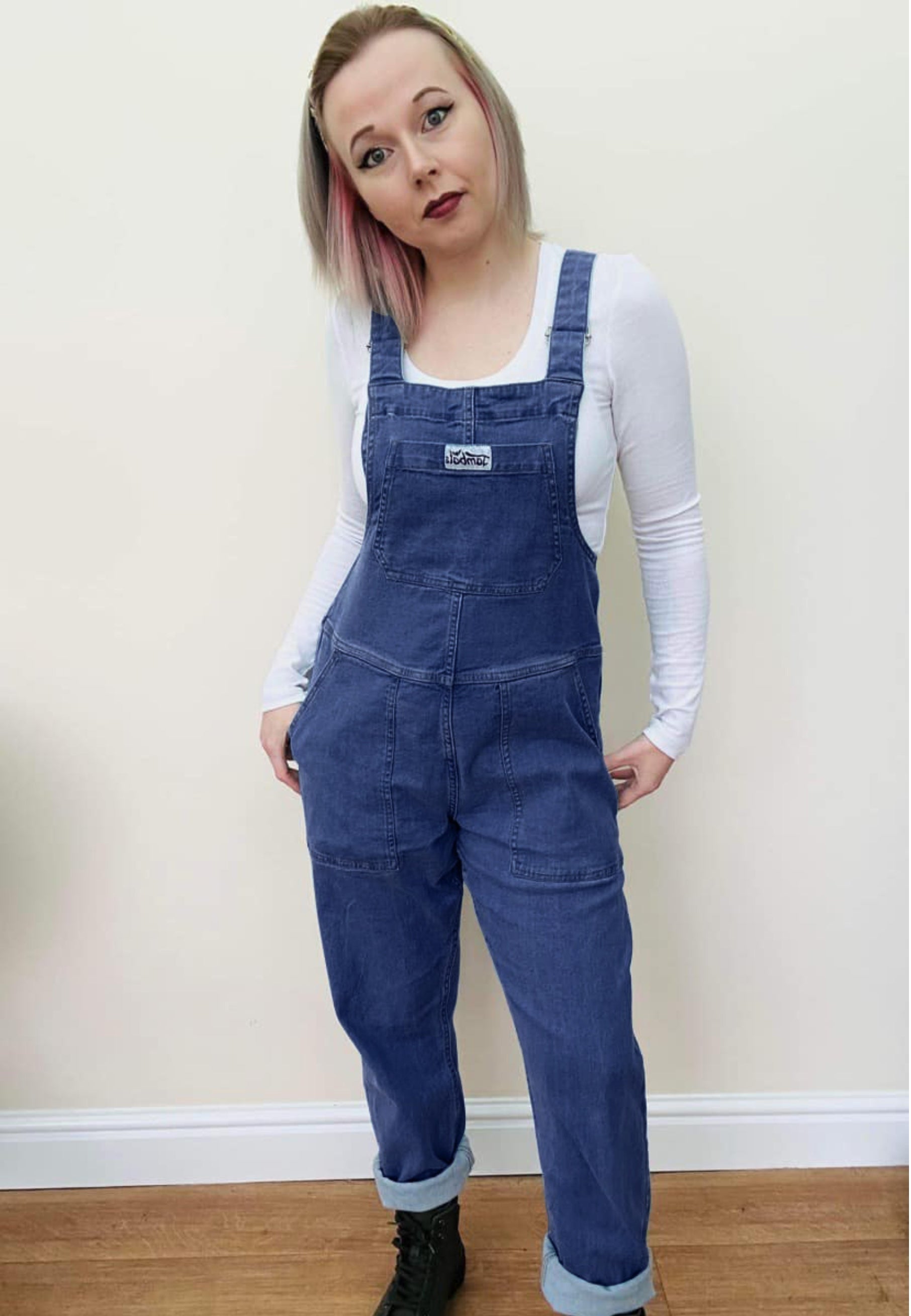 Woman wearing dark denim dungarees and a white top. 