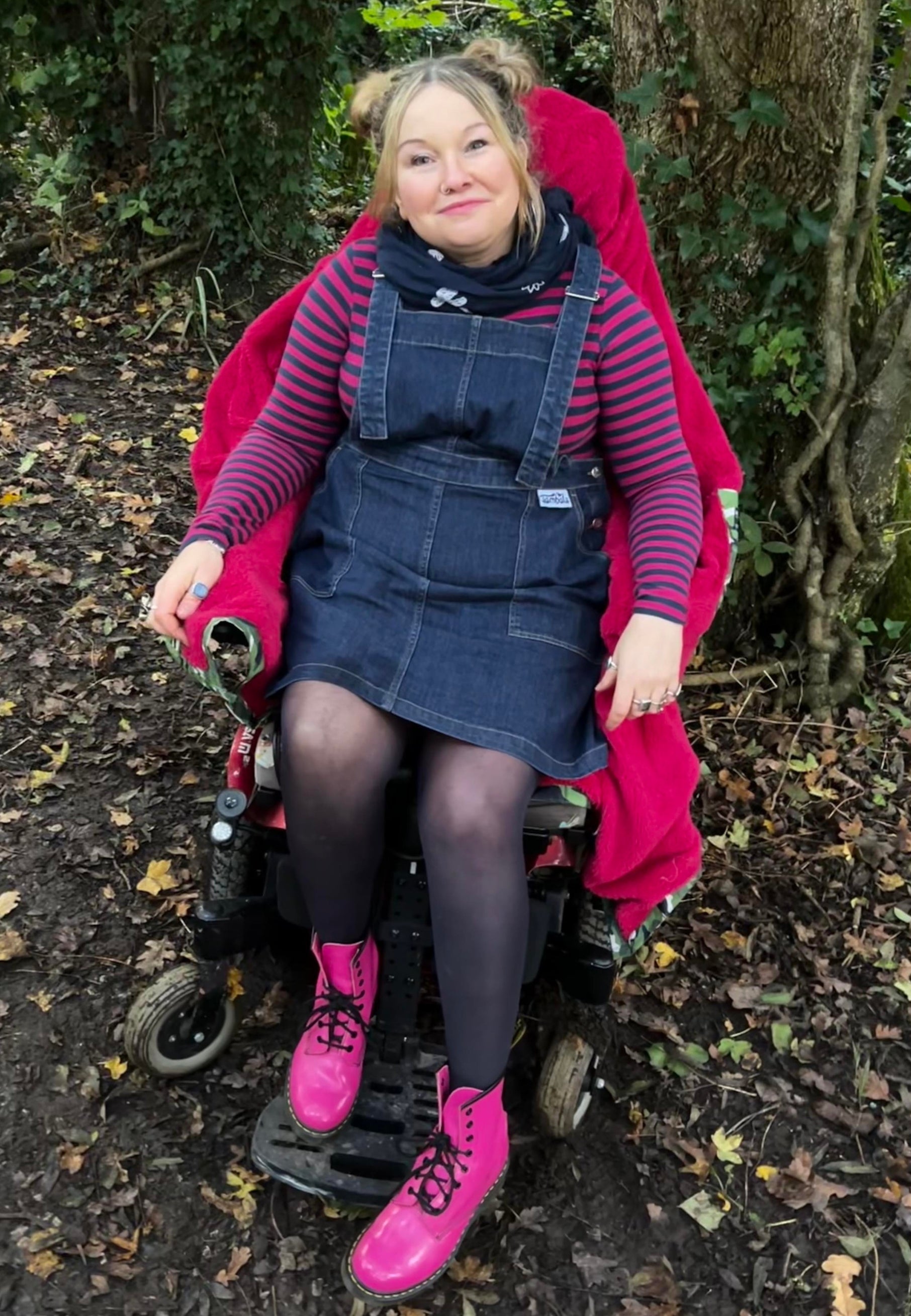 Woman in a wheelchair wearing a dark denim pinafore and pink Dr Martens boots. 