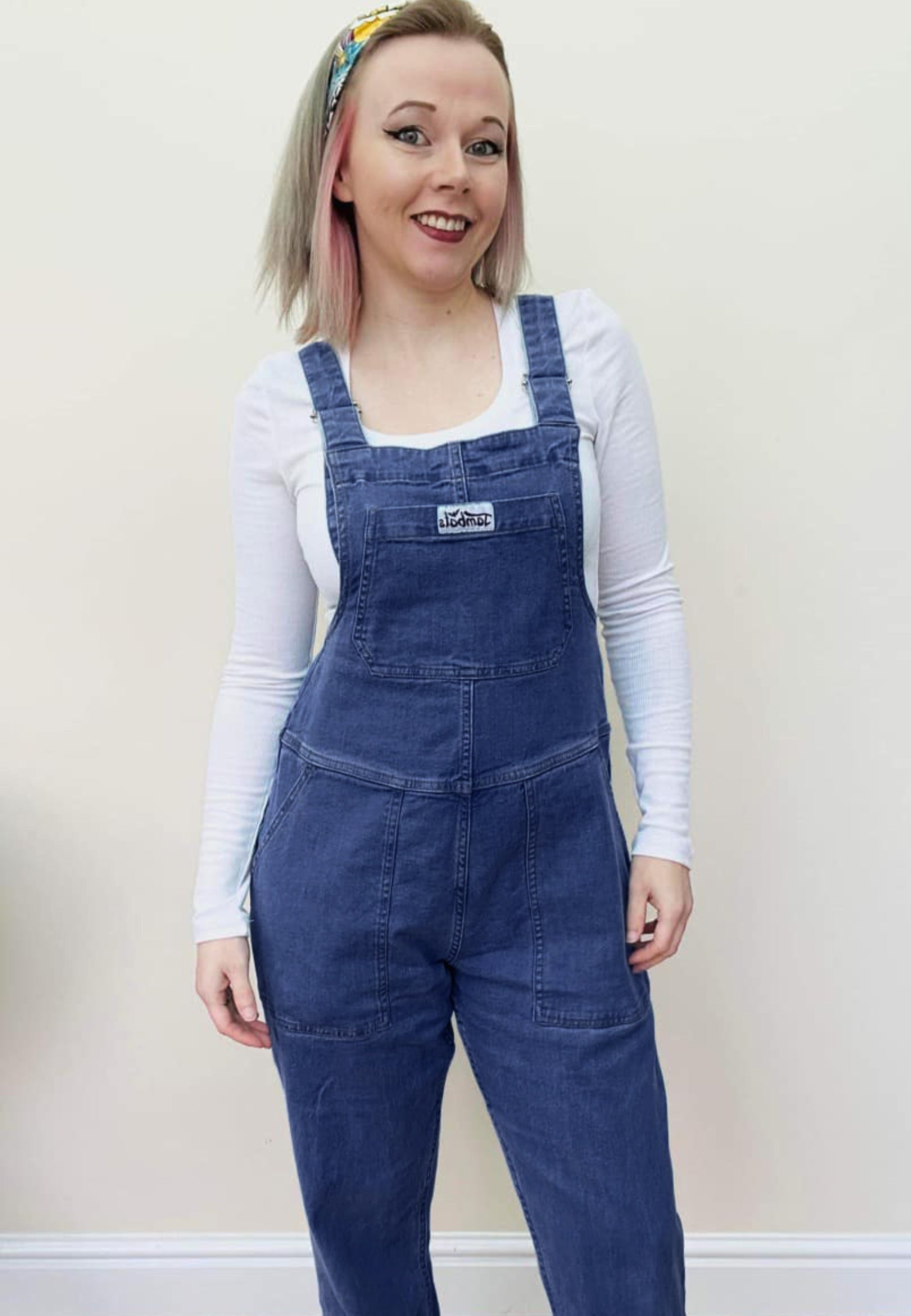 Woman wearing dark denim dungarees and a white top. 