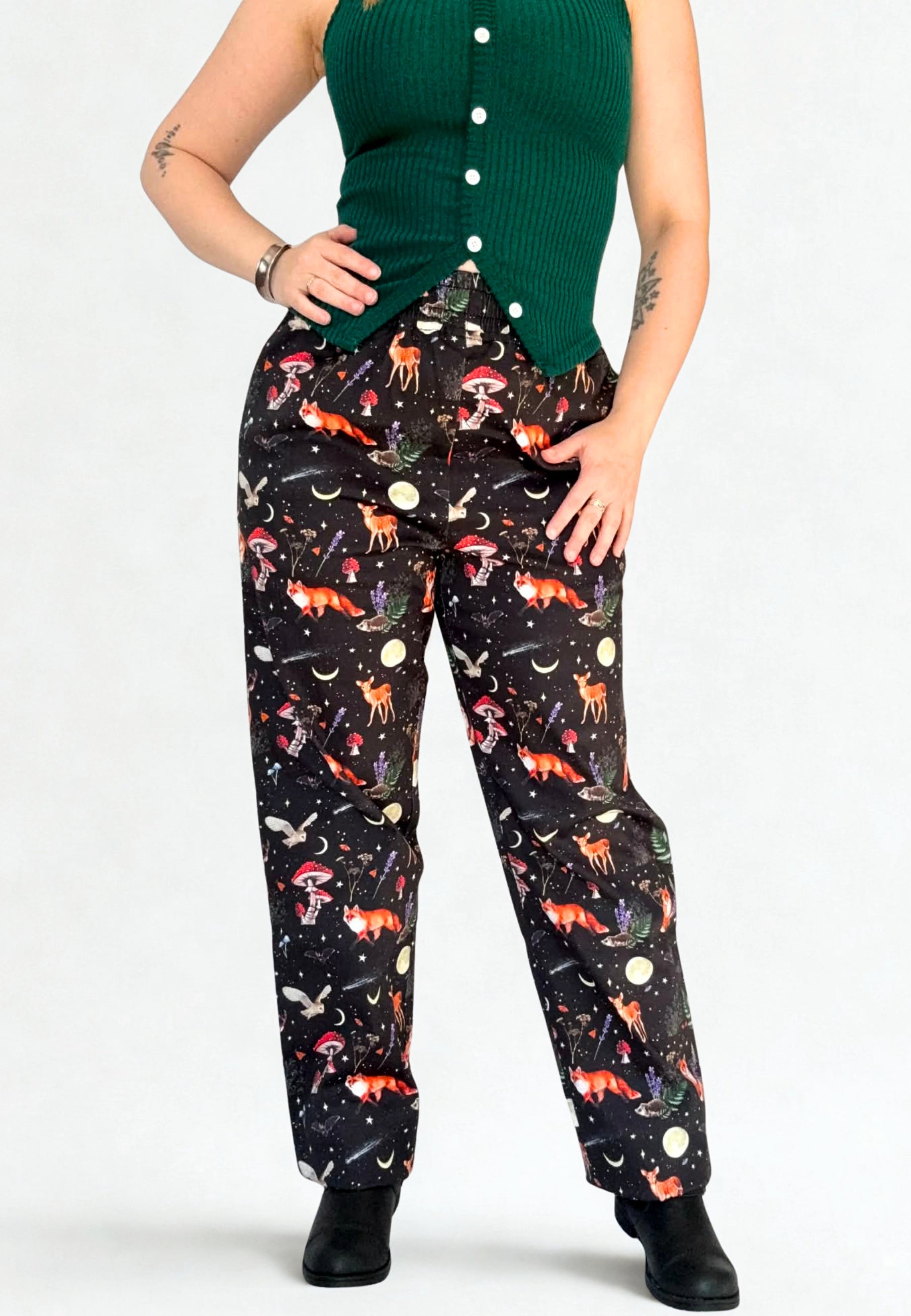 Person wearing black pants with fox and moon and dark forest pattern against a white background