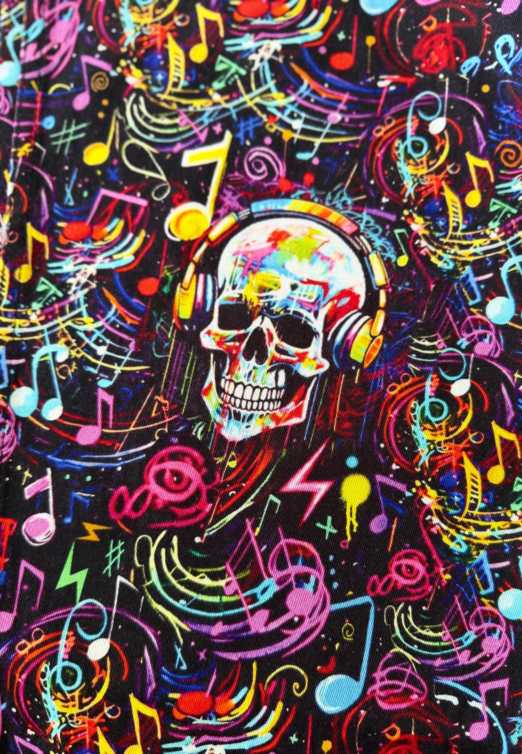 A vibrant, multicolored graphic print featuring a central skull wearing headphones, surrounded by an energetic pattern of neon musical notes, lightning bolts, and abstract scribbles on a black background.