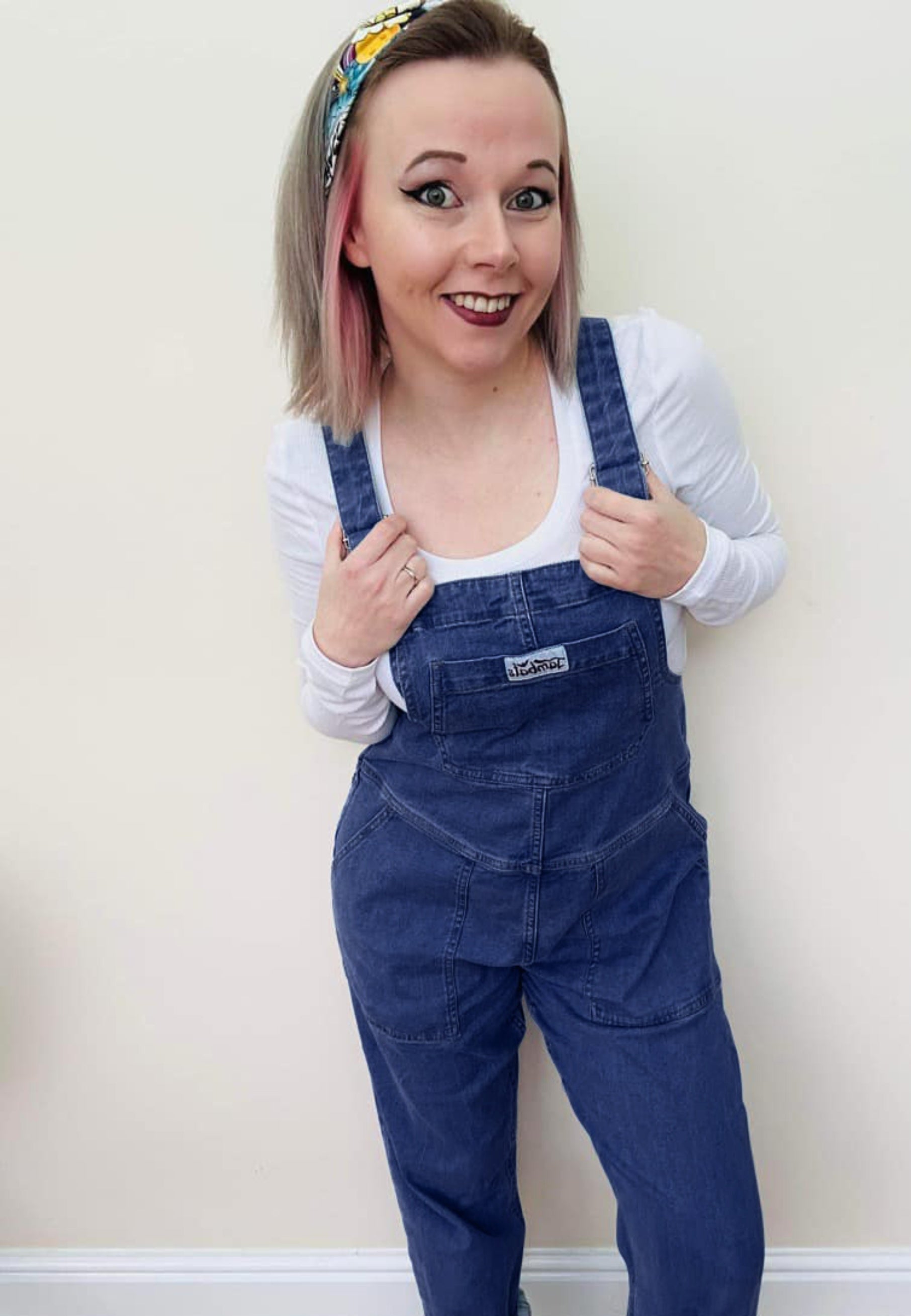 Woman wearing dark denim dungarees and a white top. 