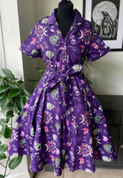 A beautiful purple shirt dress with a floral and celestial pattern, showing the 4 elements and celebrating natures magic. Featuring a button-up front, a self-fabric belt, and hip pockets, displayed on a mannequin.