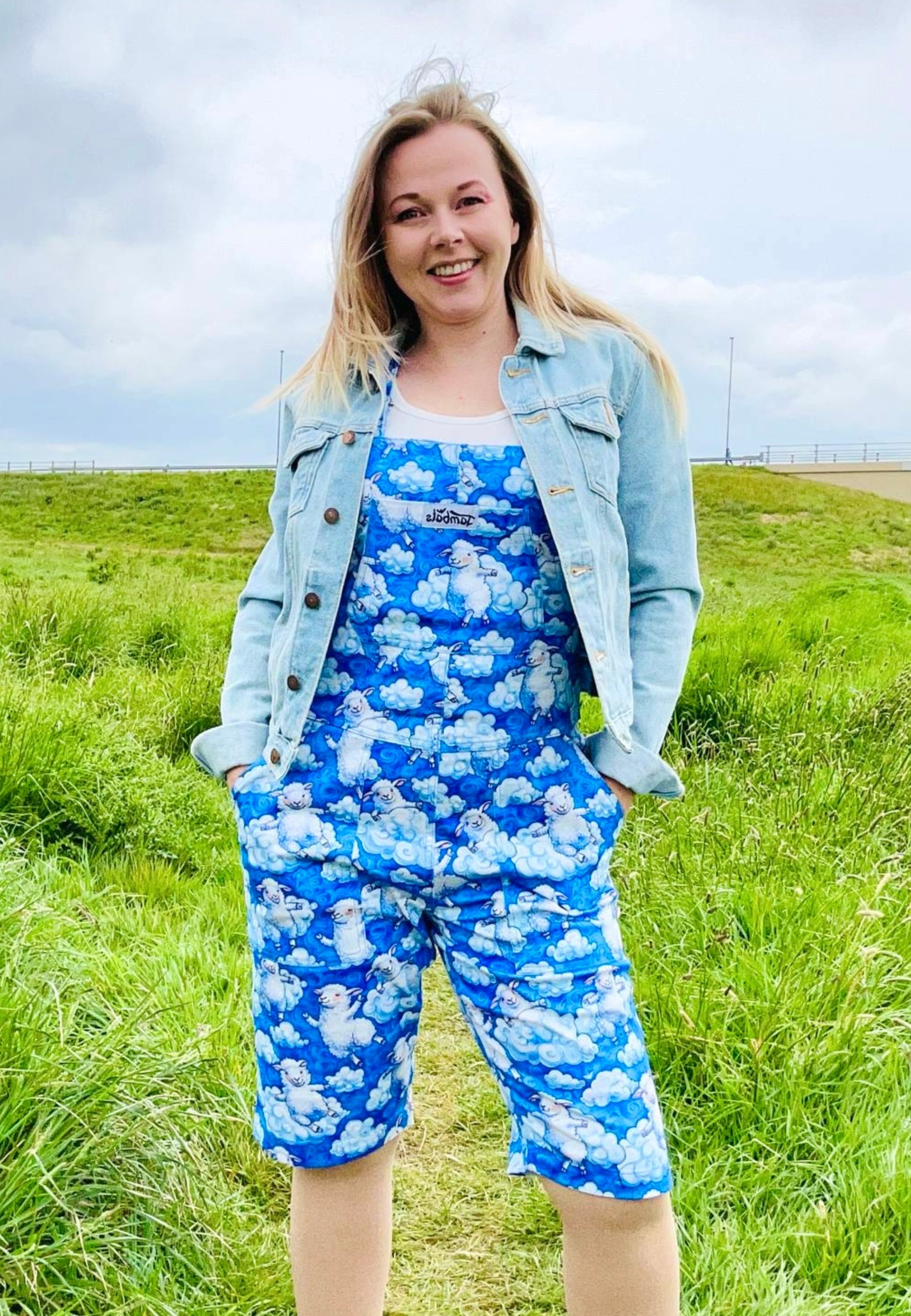 Model wearing a blue and white fluffy cloud and sheep dungarees. Outdoor photo with blue skies and clouds. 