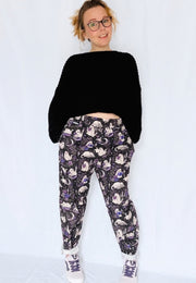 A woman modeling a black cropped knit sweater and black trousers with a spooky ghost cats print with white sneakers, standing against a plain light background.