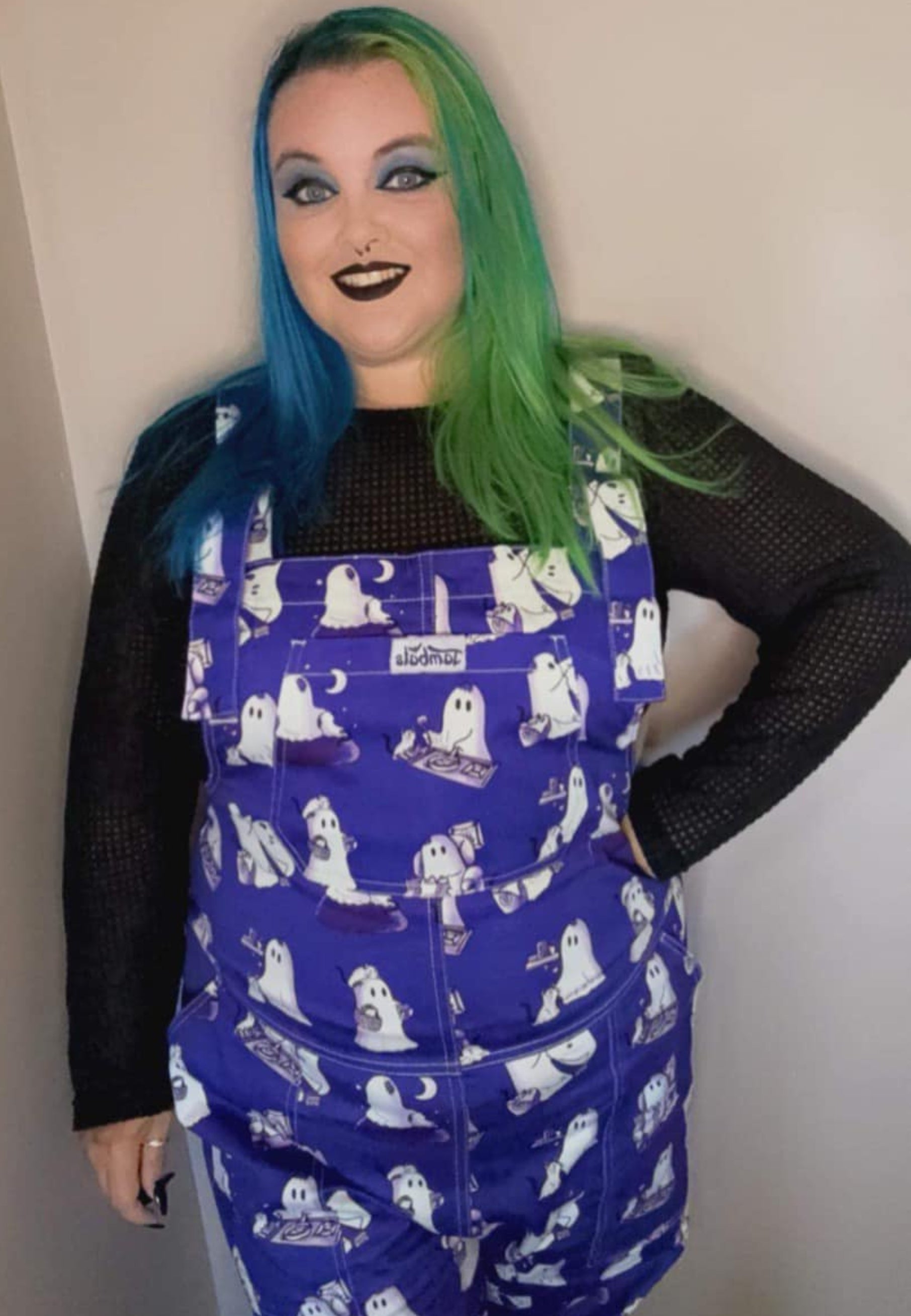 A woman wearing cute blue dungarees with a print of ghosts and ghost cats. 