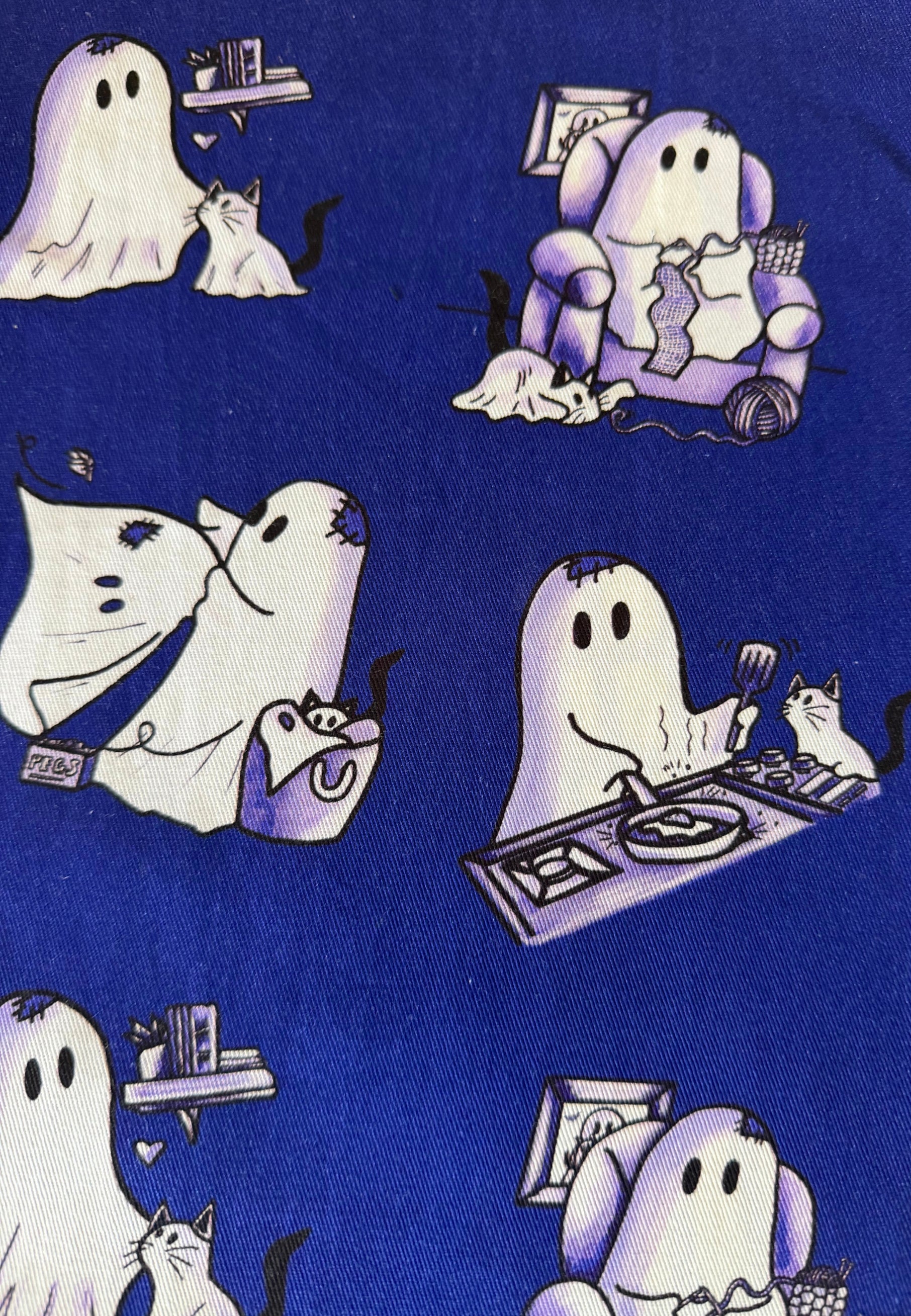 A close-up of a blue fabric with a repeating cute pattern of white ghosts and ghost cats in various playful poses.