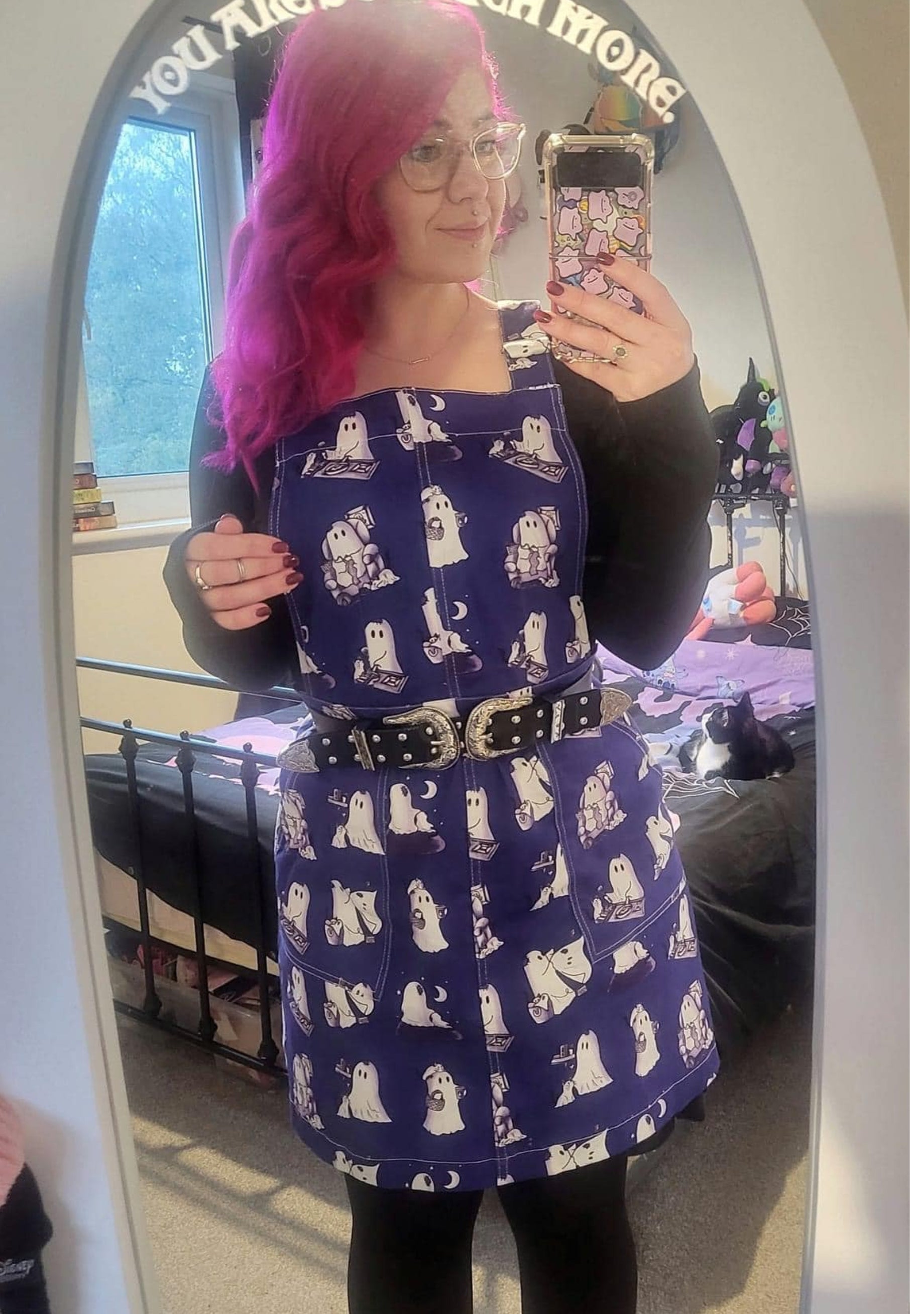 Woman wearing a beautiful blue pinafore with cute images of ghosts and ghost cats doing everyday things. Jambats January Sale. 
