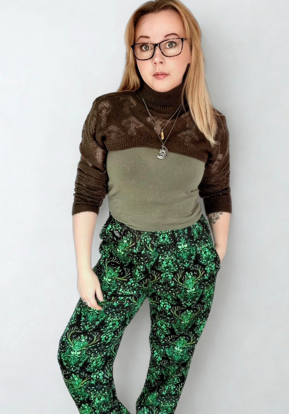 Woman wearing a brown sweater with a green top and black trousers with a vibrant Green Man pattern. 