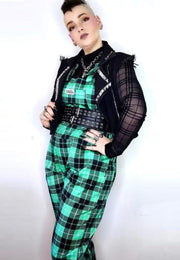 Model wearing green tartan dungarees, paired with a black mesh top, black studded belt and boots. The dungarees have multiple pockets and the person has their hand on their hips. Alternative punk goth style