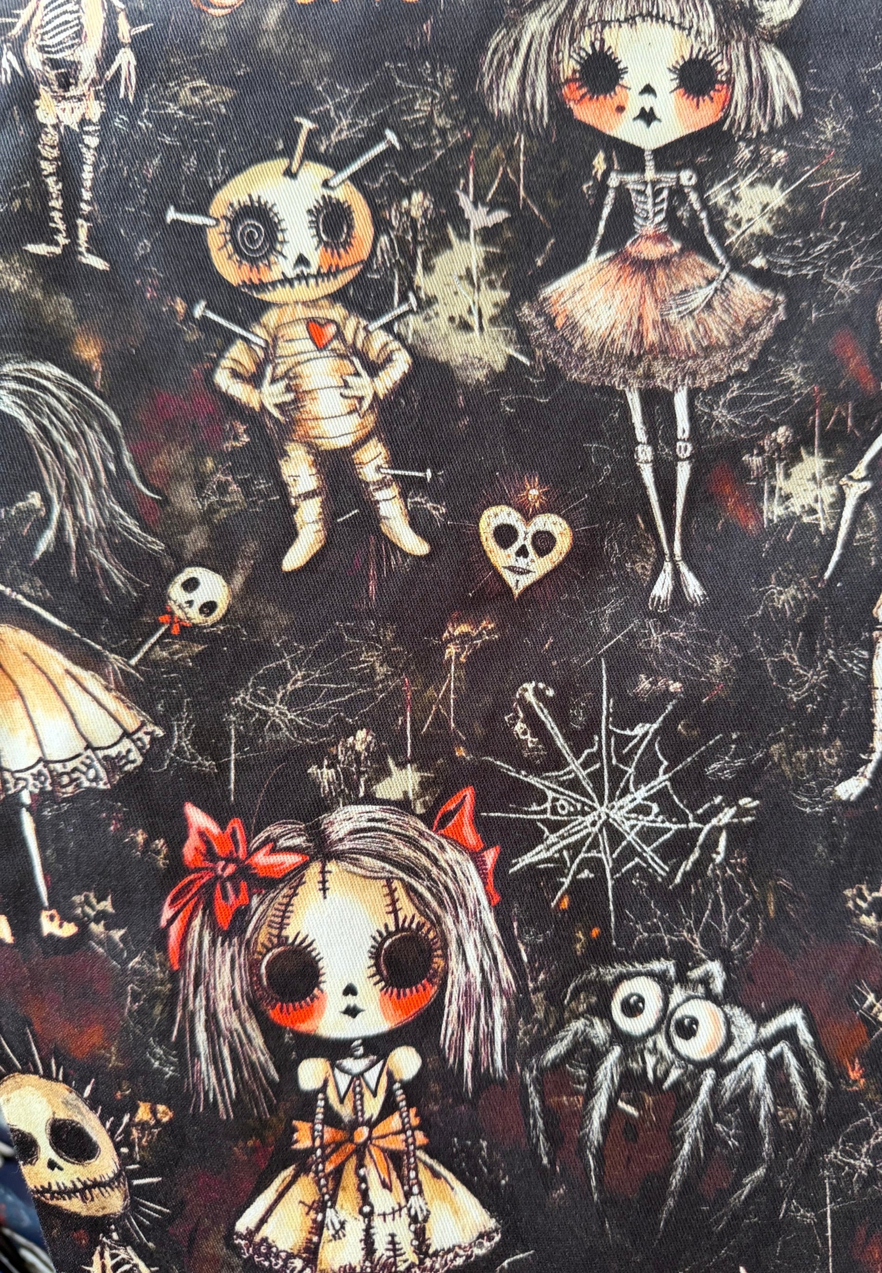 Gothic fabric pattern featuring illustrated dolls, skulls, spiders, bones, and web motifs on a dark background.