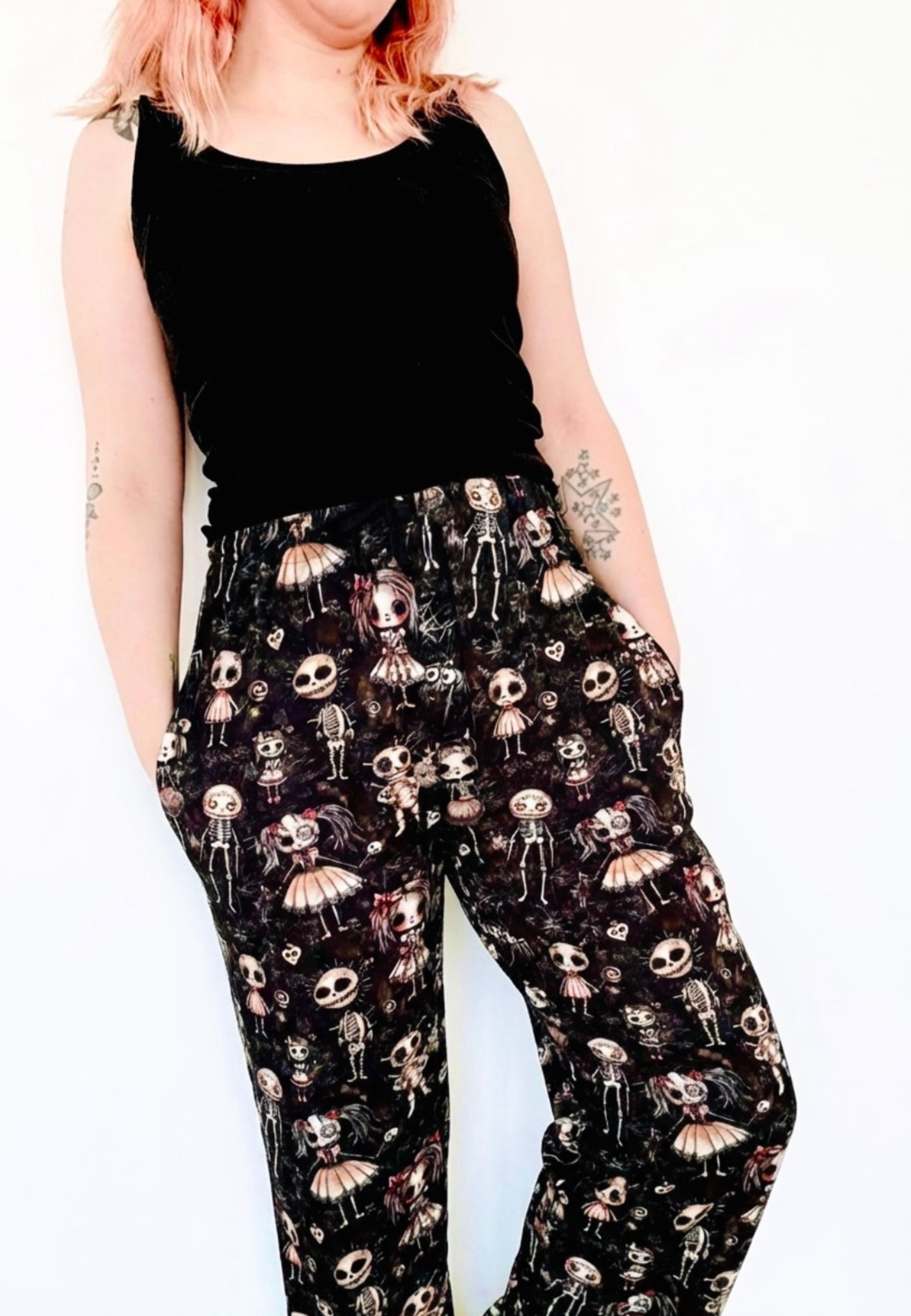 Woman wearing a black sleeveless top and patterned lounge pants with haunted dolls print.