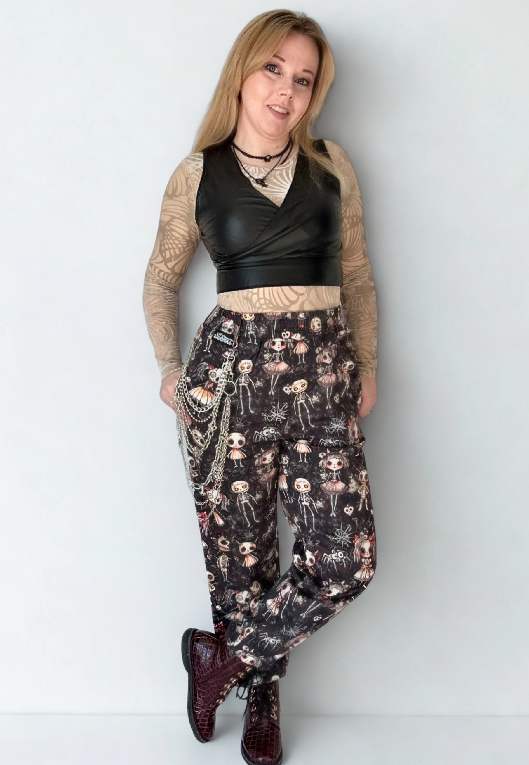 Woman wearing a black leather top and gothic Haunted Dolls patterned trousers on a white studio background