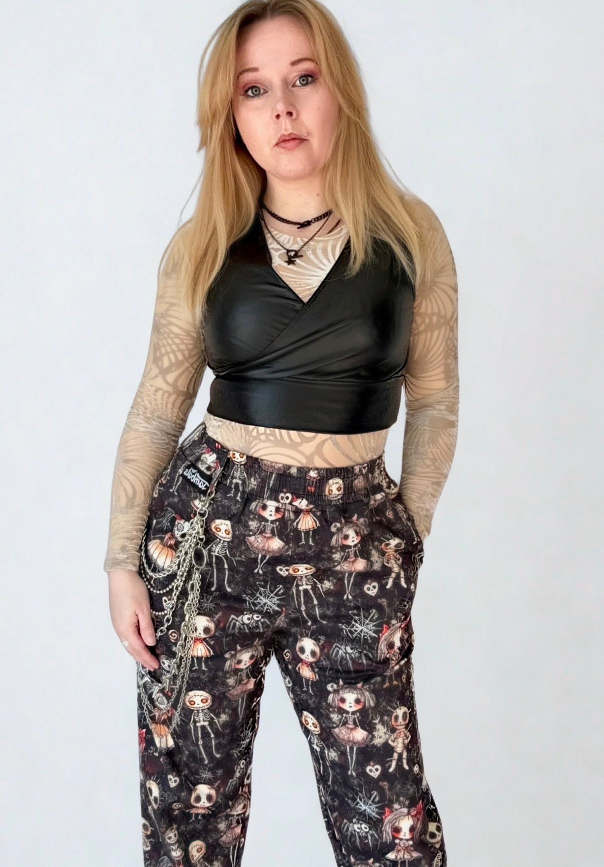 Woman wearing a black leather top and gothic Haunted Dolls patterned trousers on a white studio background