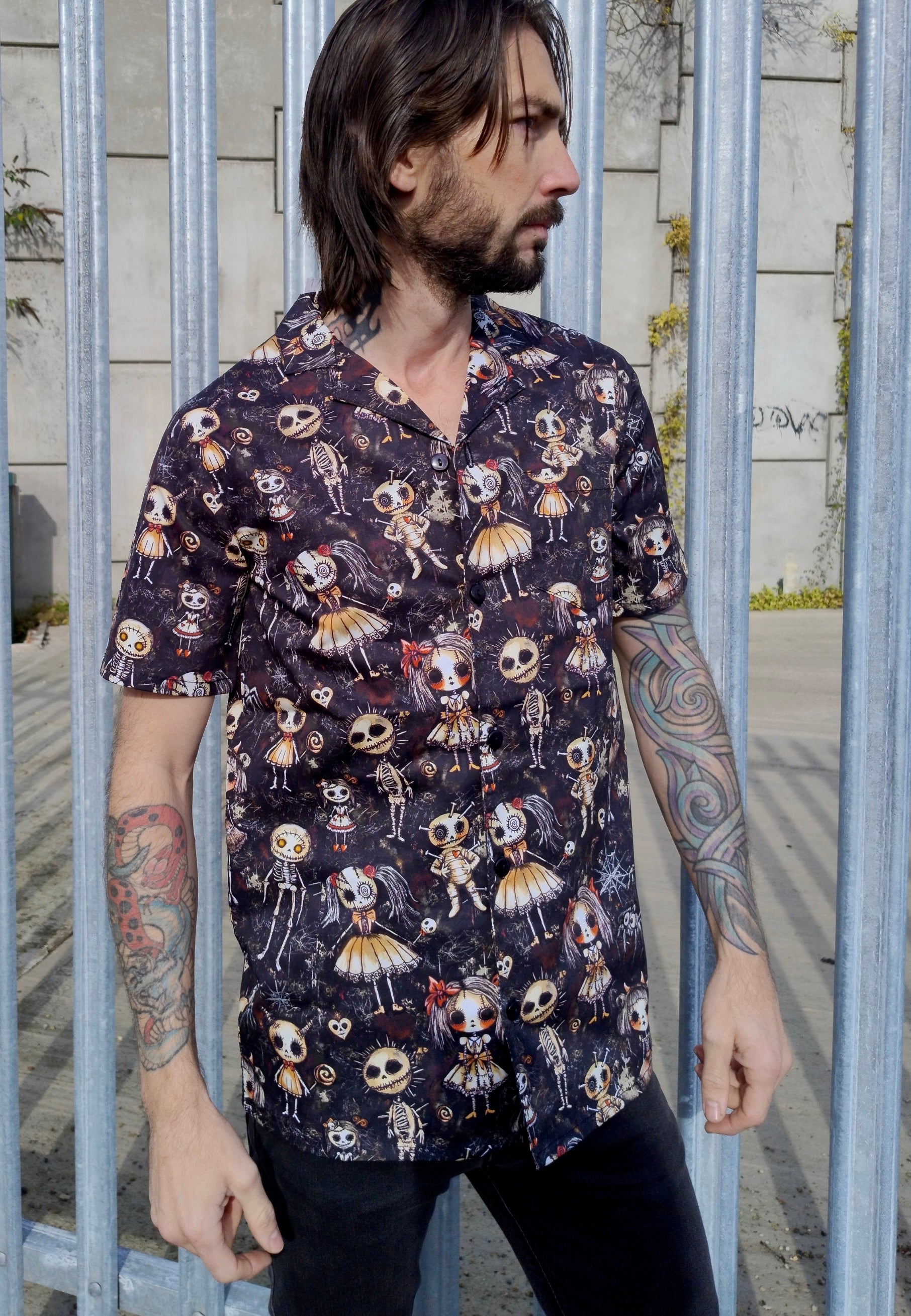 Man in a shirt with a Haunted Dolls print. Man is outdoors by an abandoned warehouse. 