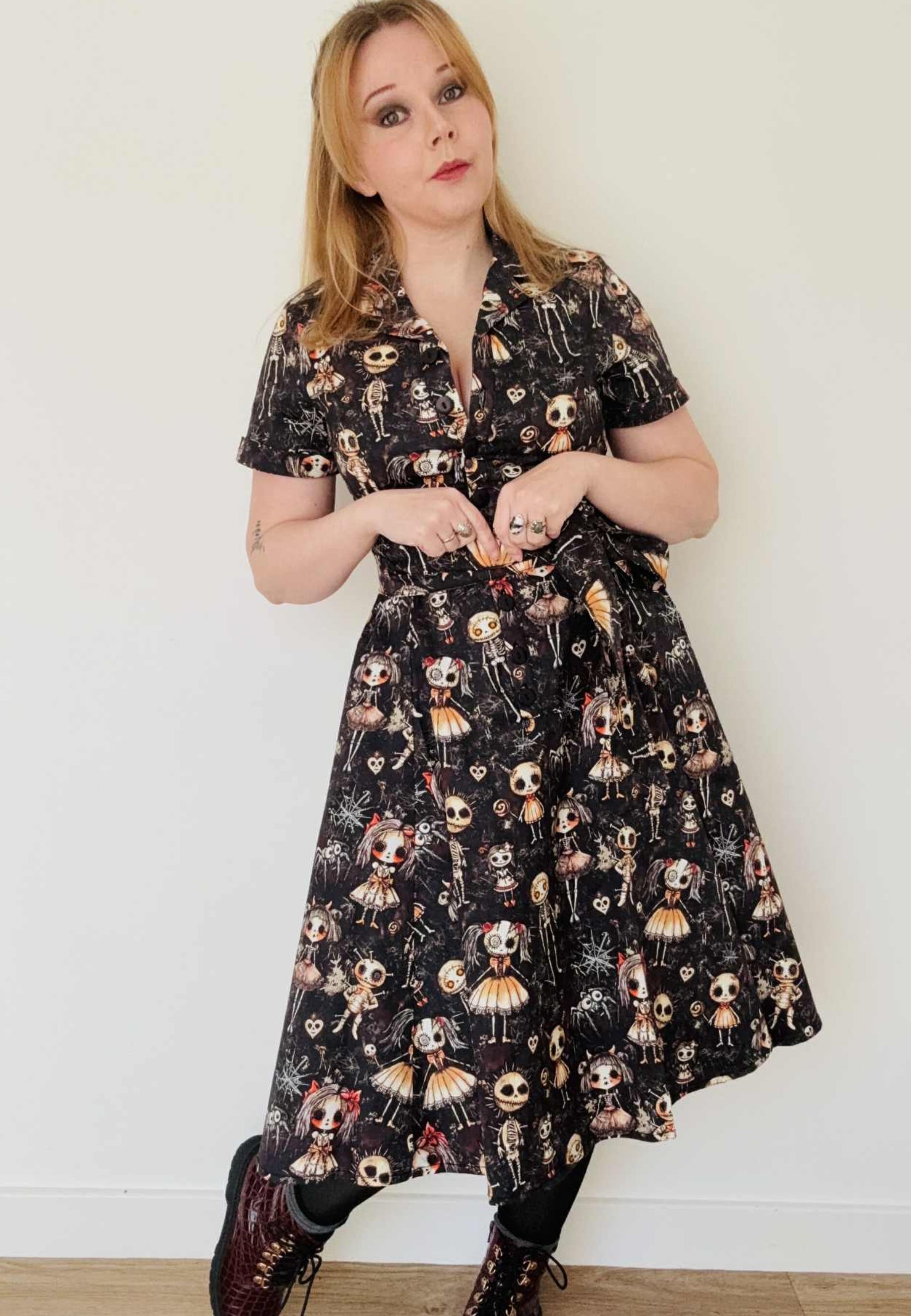 Woman wearing a shirt dress with a fabulous Haunted dolls print and boots. Quirky pose. Studio photo. 
