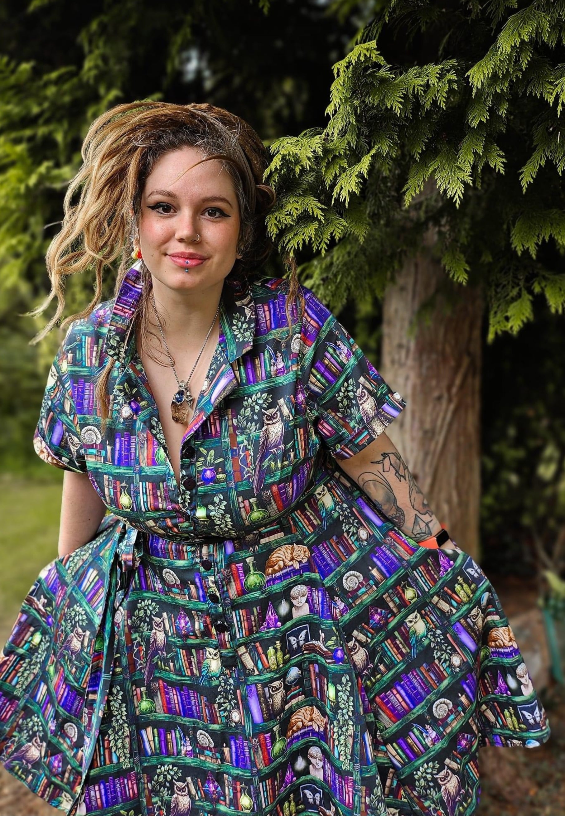 Woman wearing a beautiful shirt dress with a bookcase print, featuring a button-up bodice, a full skirt, and a tied belt at the waist. Magical Dark academia bookcase print. 