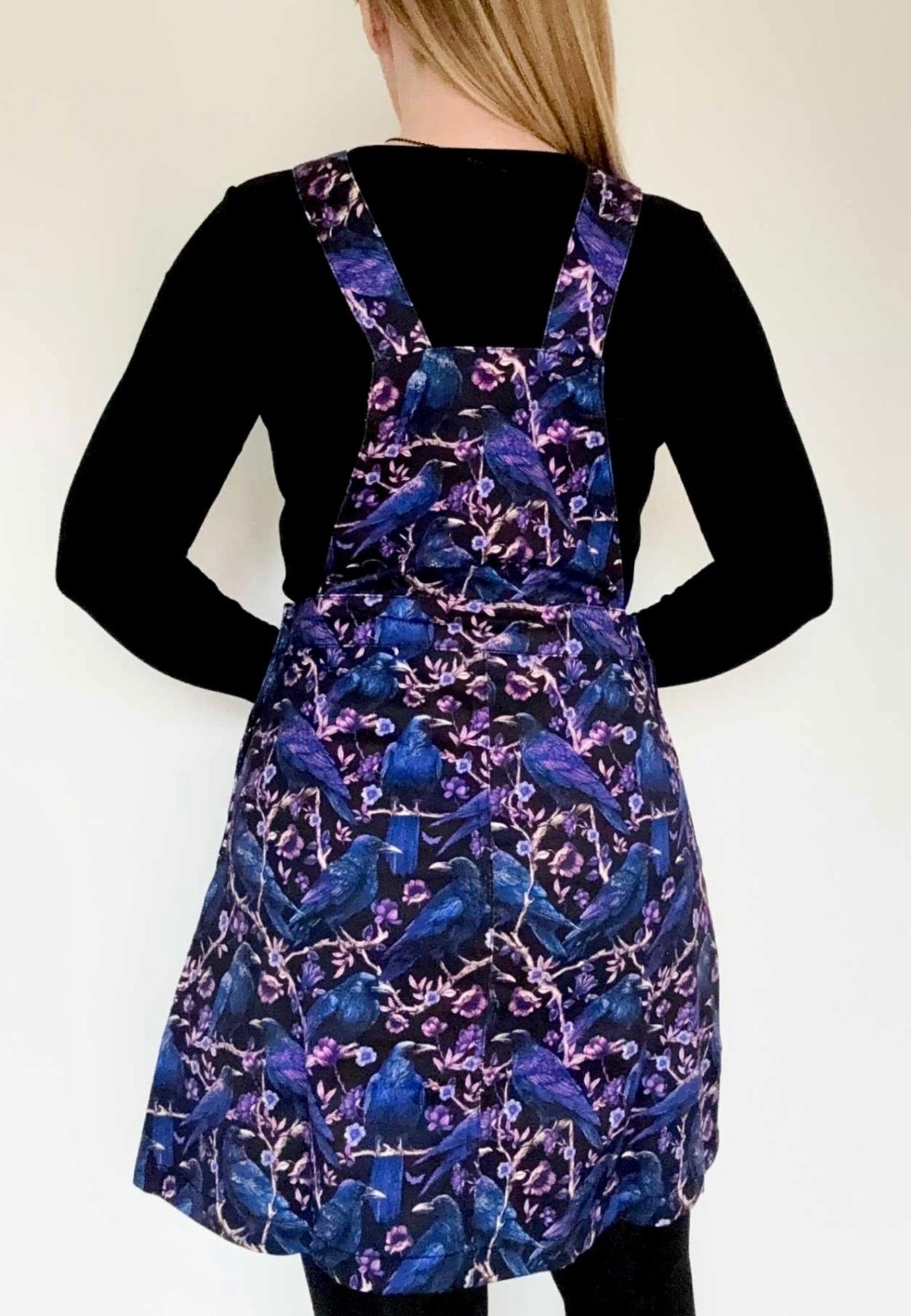 Back view of a woman wearing a pinafore with a beautiful print of Corvids, crows and ravens. Studio photo 