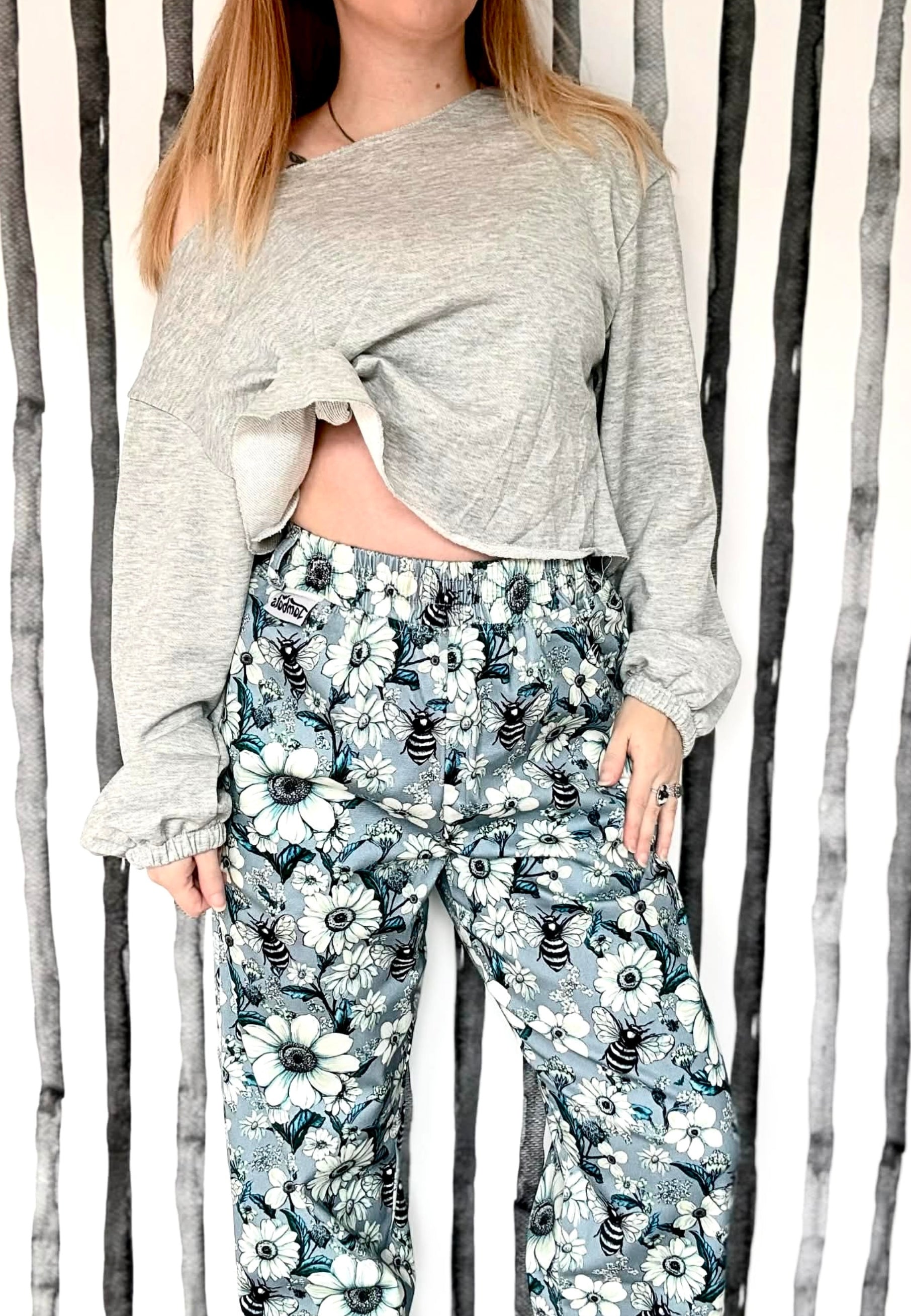 Person wearing a gray long sleeve slouchy top and floral pants against a striped background