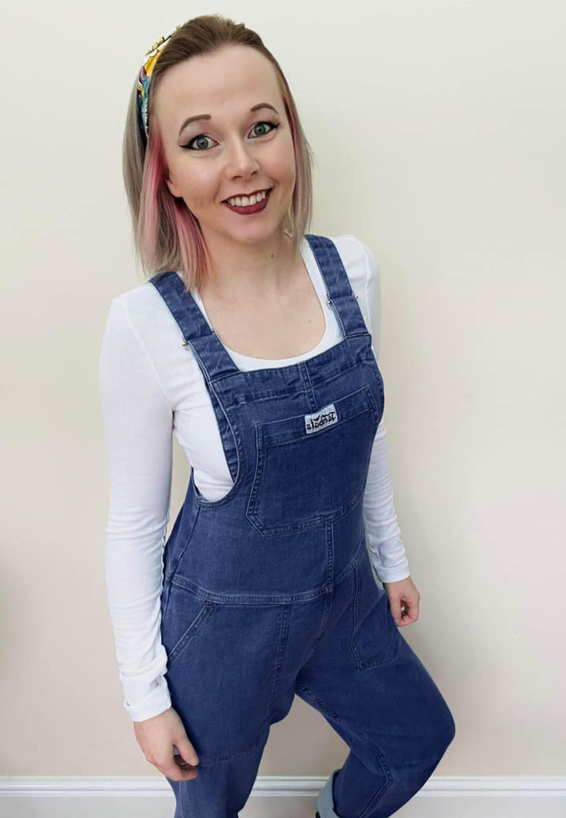 Woman wearing dark denim dungarees and a white top. 