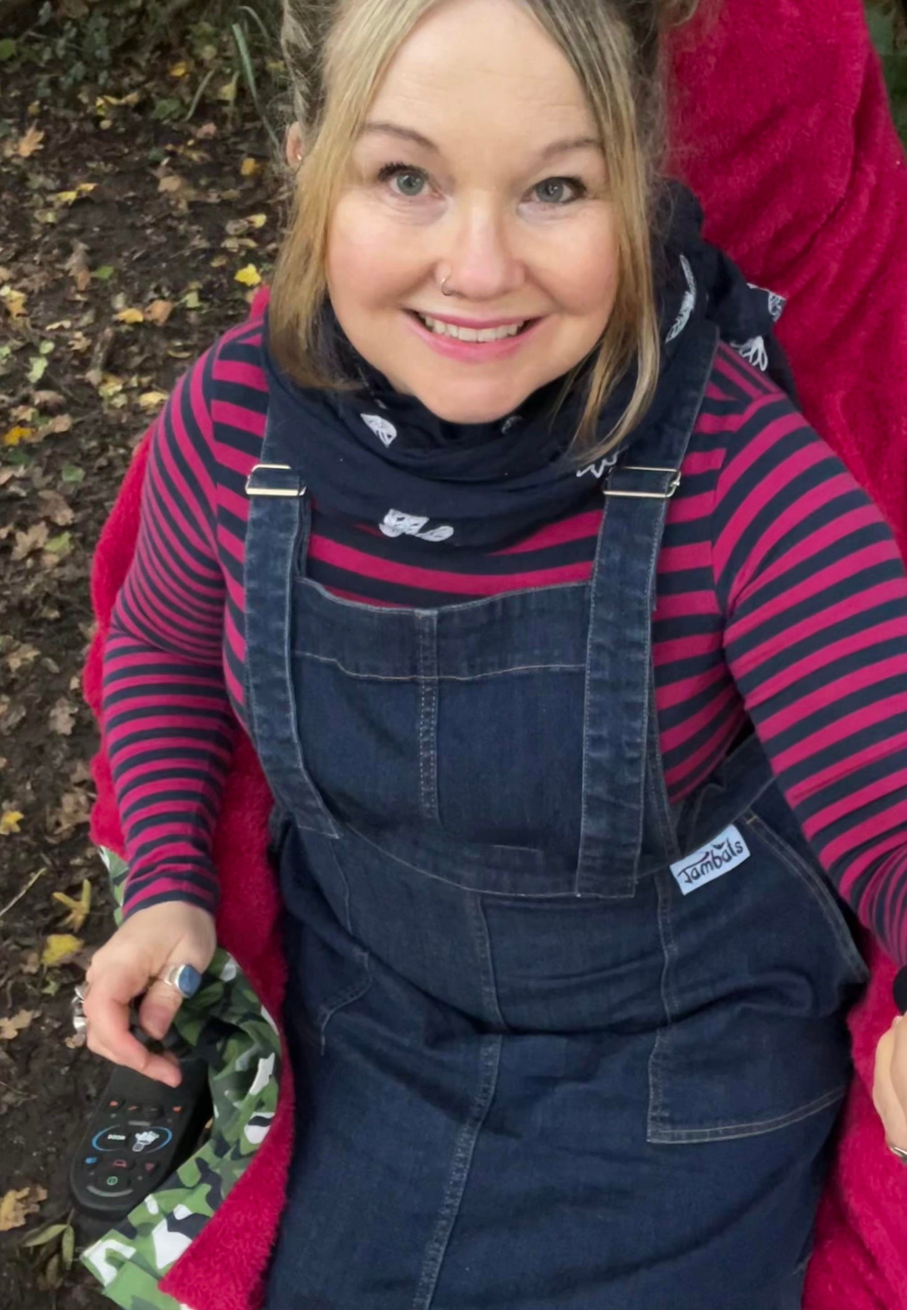 Woman in a wheelchair wearing a dark denim pinafore and pink striped top. 