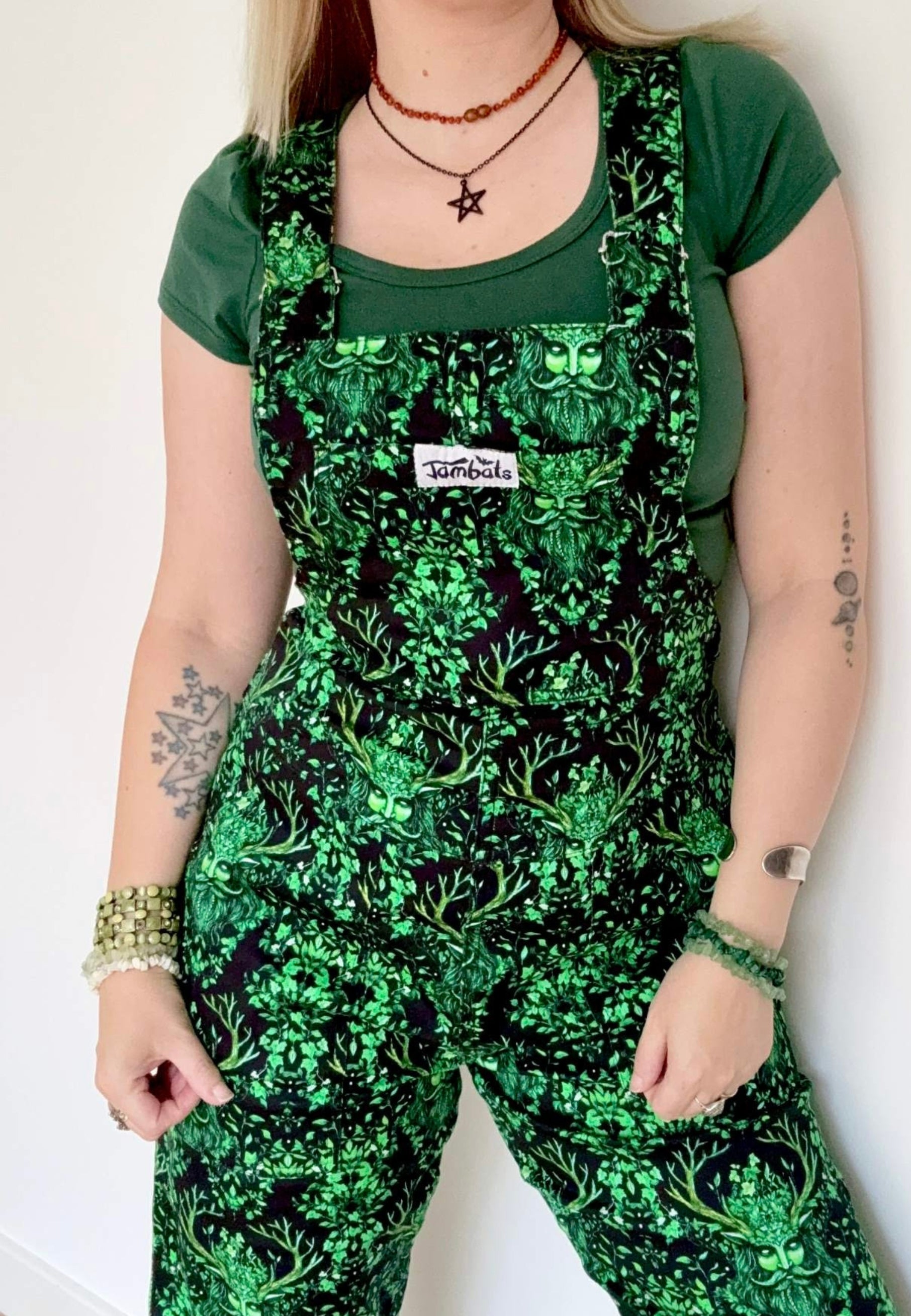 Woman  wearing black dungarees with a beautiful green man print on the dungarees. Witchy pagan style.